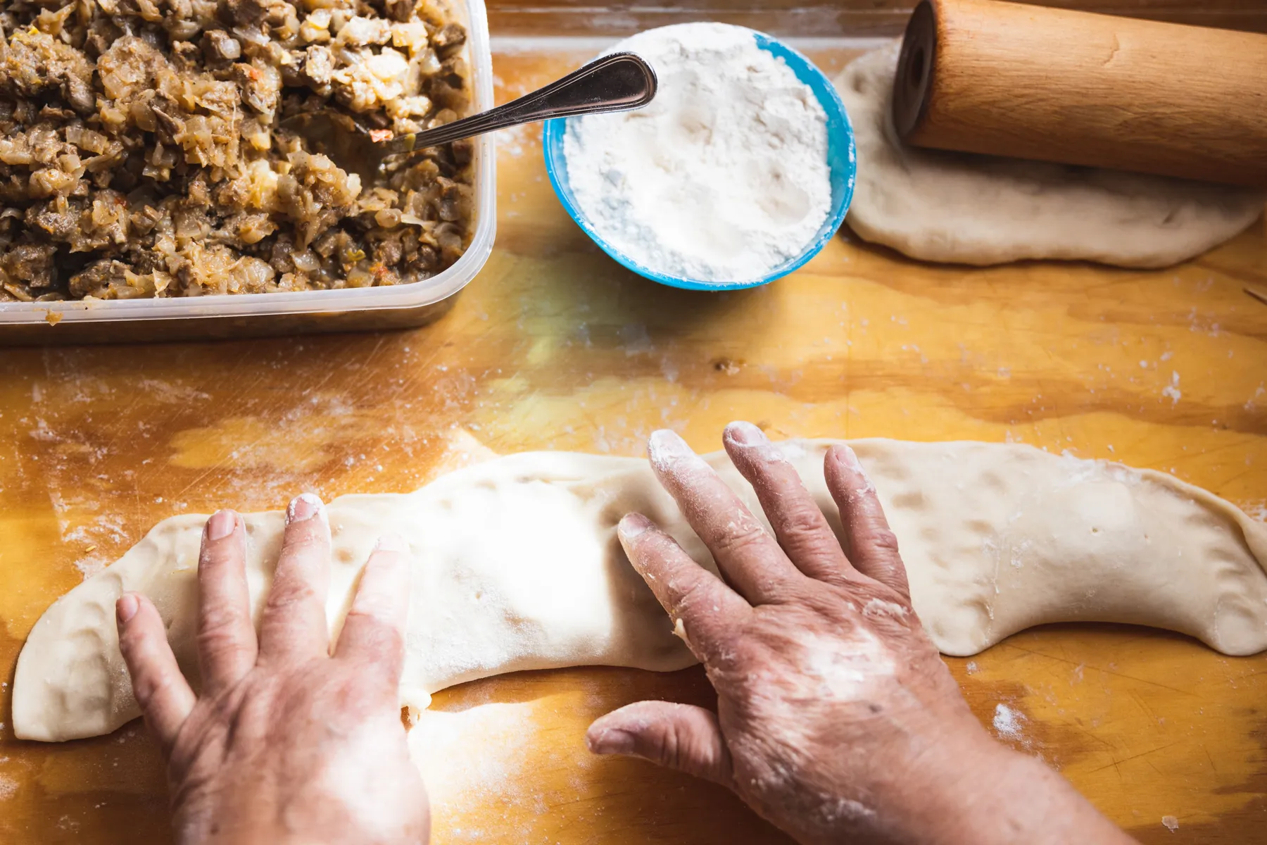 Hands shaping empanada dough around a filling
