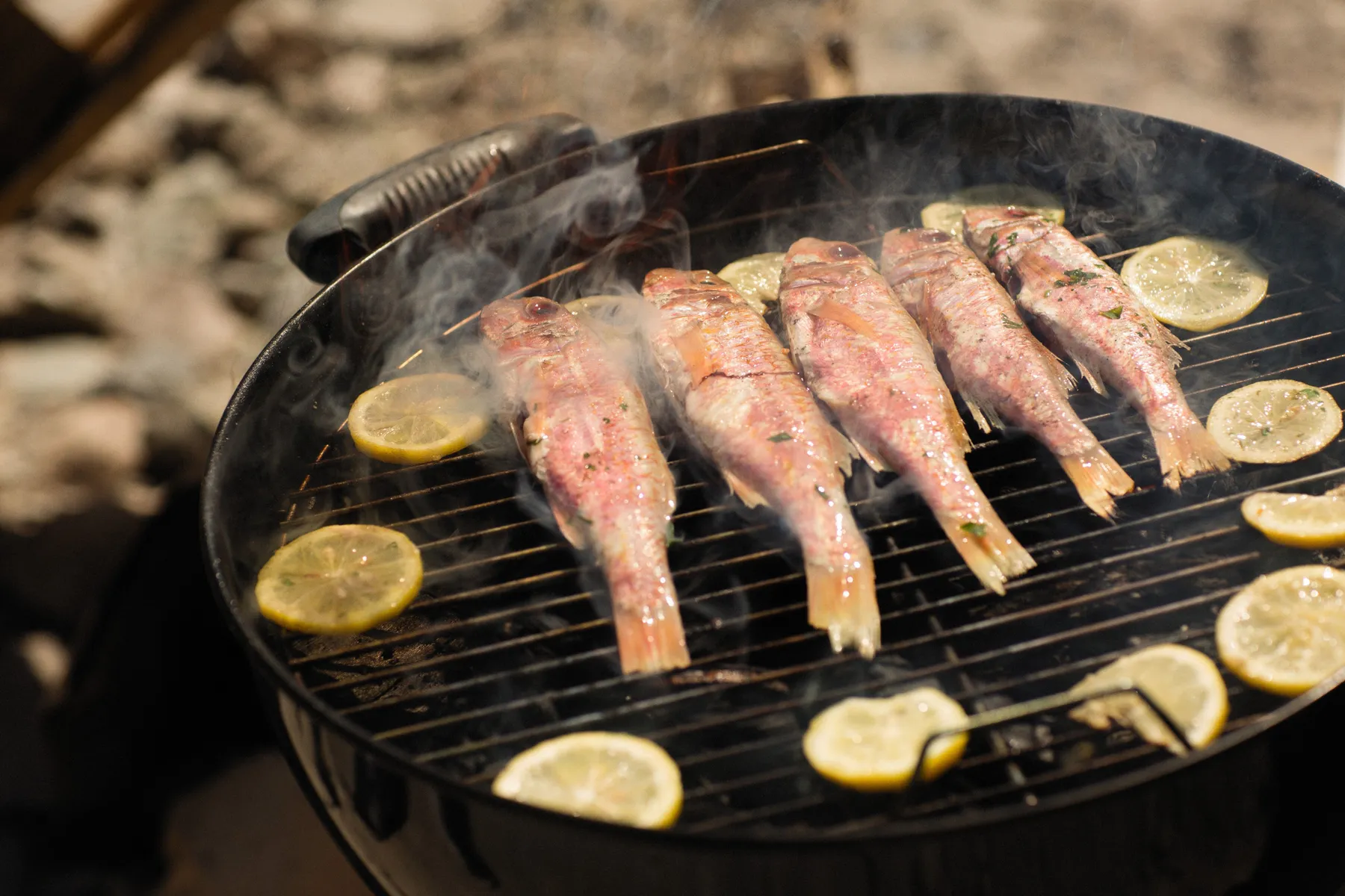 Whole fish cooking with lemon slices on a barbecue grill
