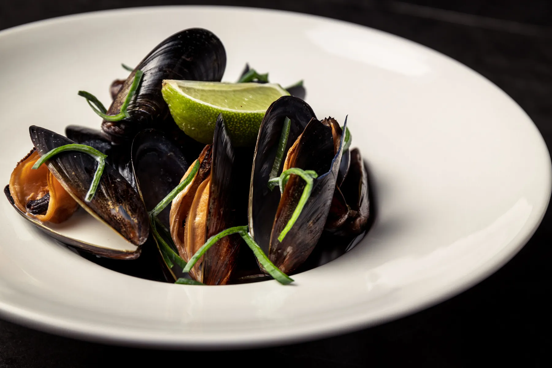 Mussels with a lime wedge on a white plate against a dark background