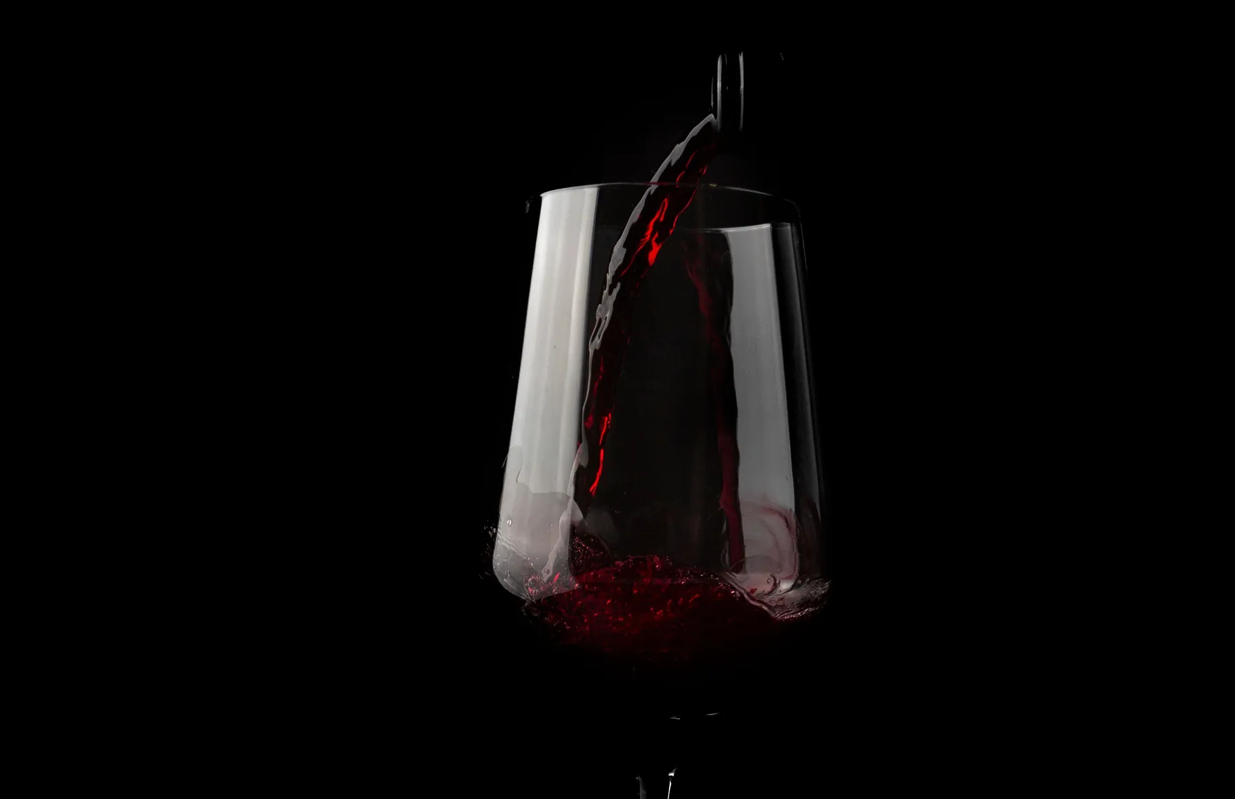 Red wine pouring into a glass against a dark background