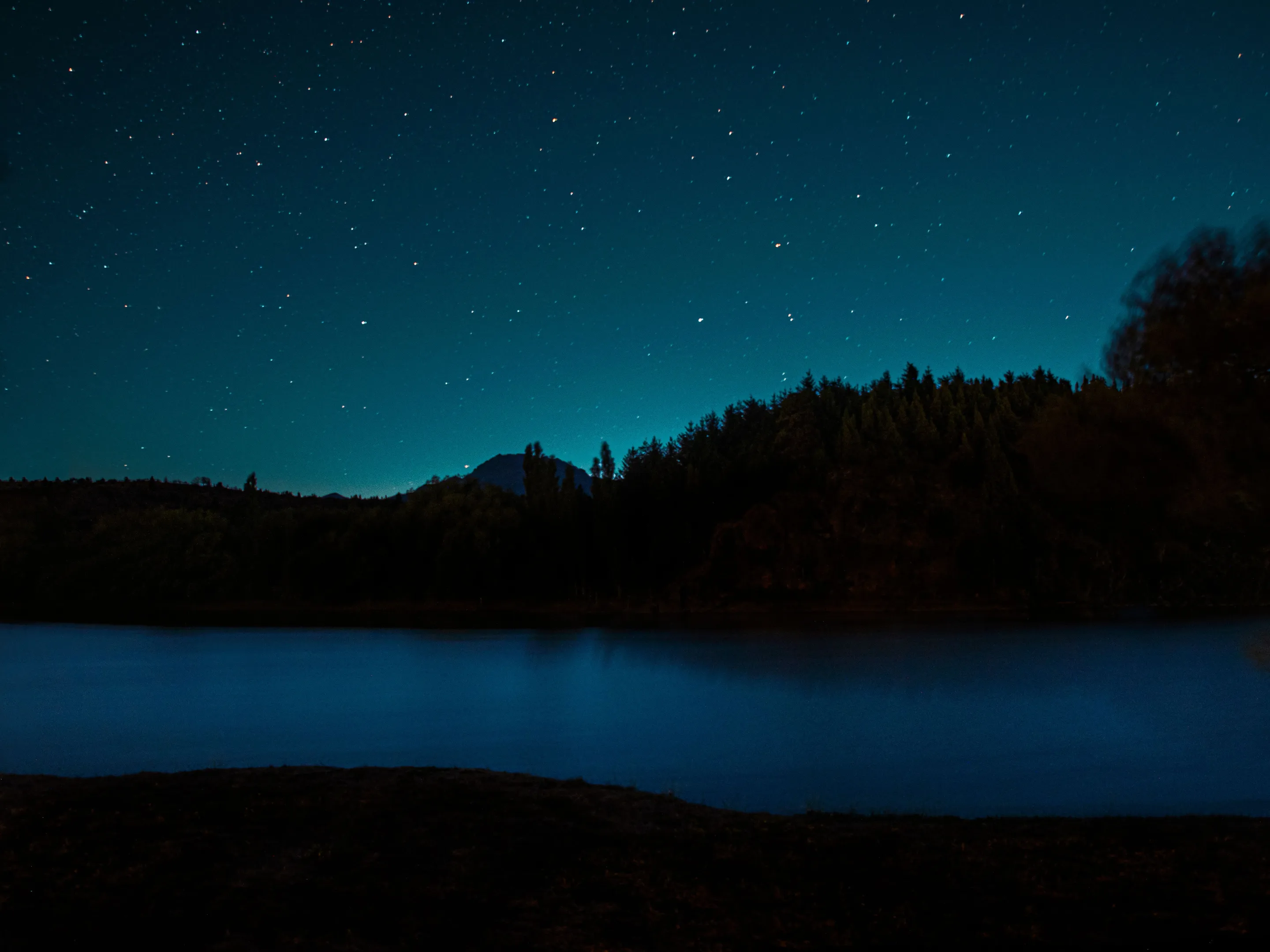 Stars above a dark mountain silhouette and lake at Trevelin