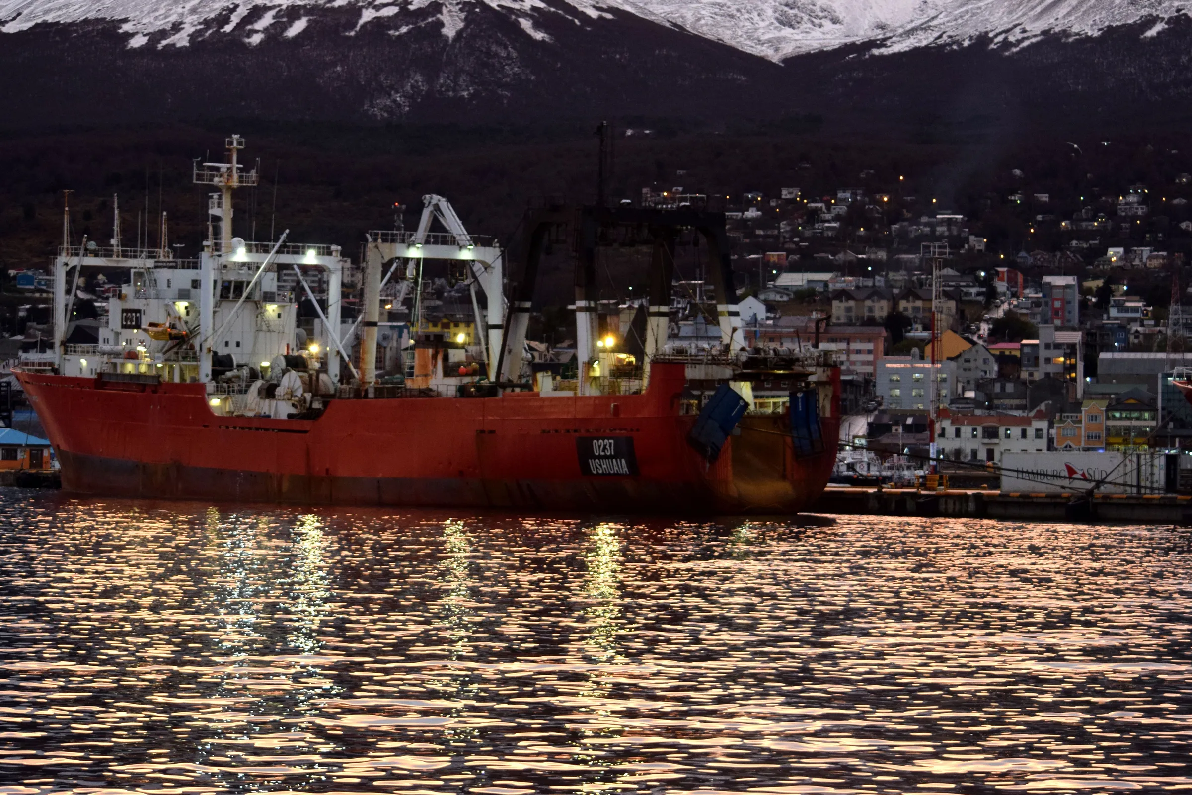 A fishing vessel in Ushuaia harbour with evening light and snowy mountains