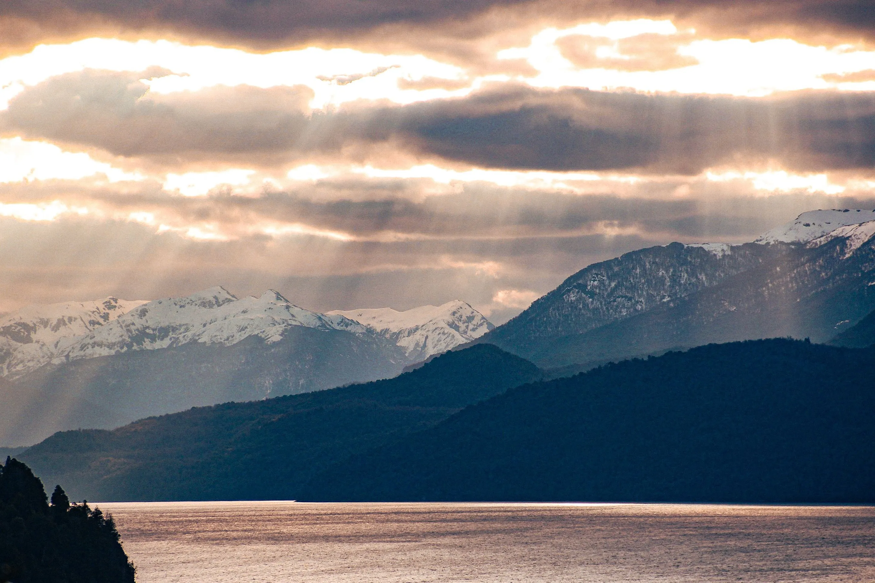 Sunbeams breaking through cloud above snowy mountains and lake water