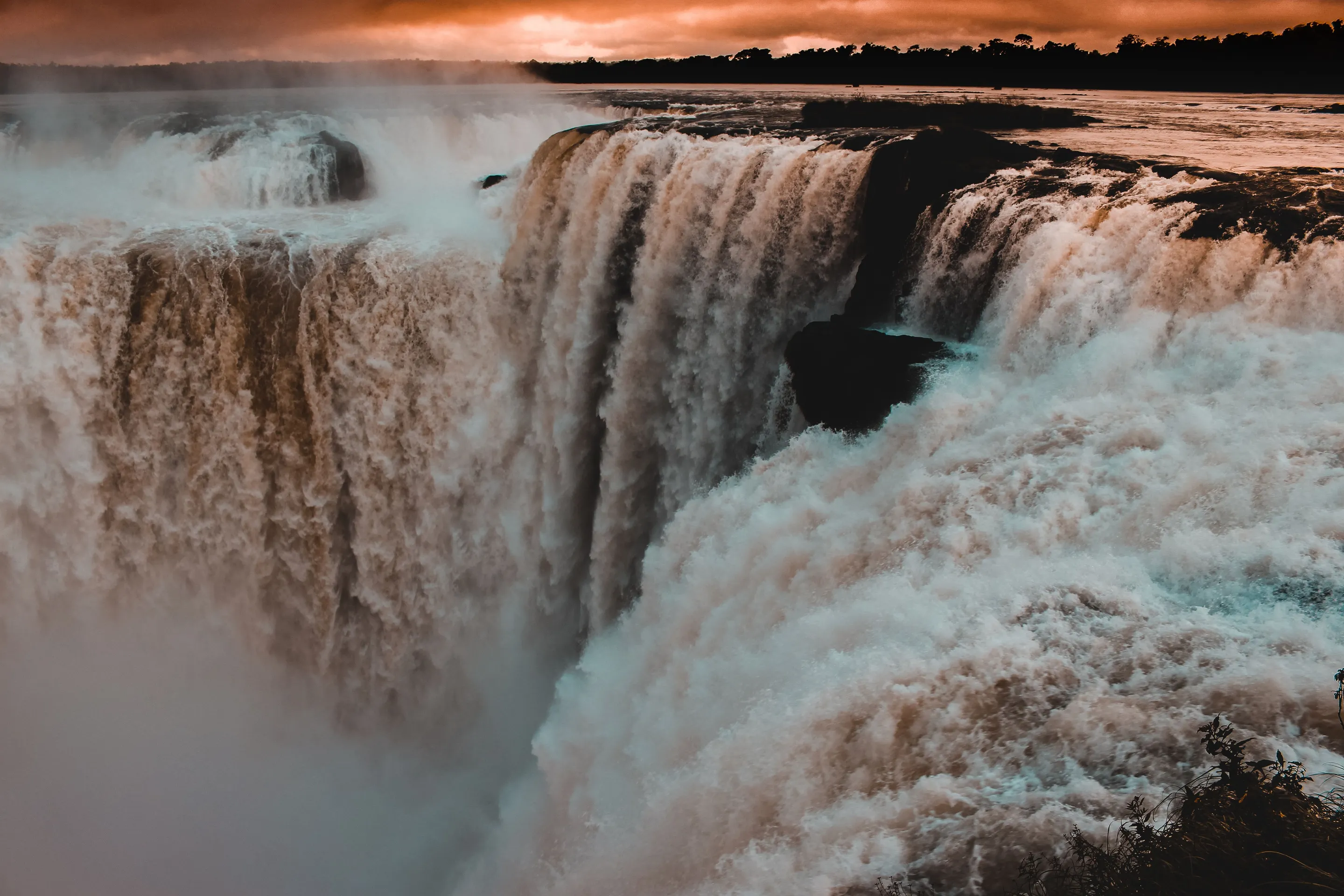 Water pouring into the Iguazú gorge beneath warm light and rising mist
