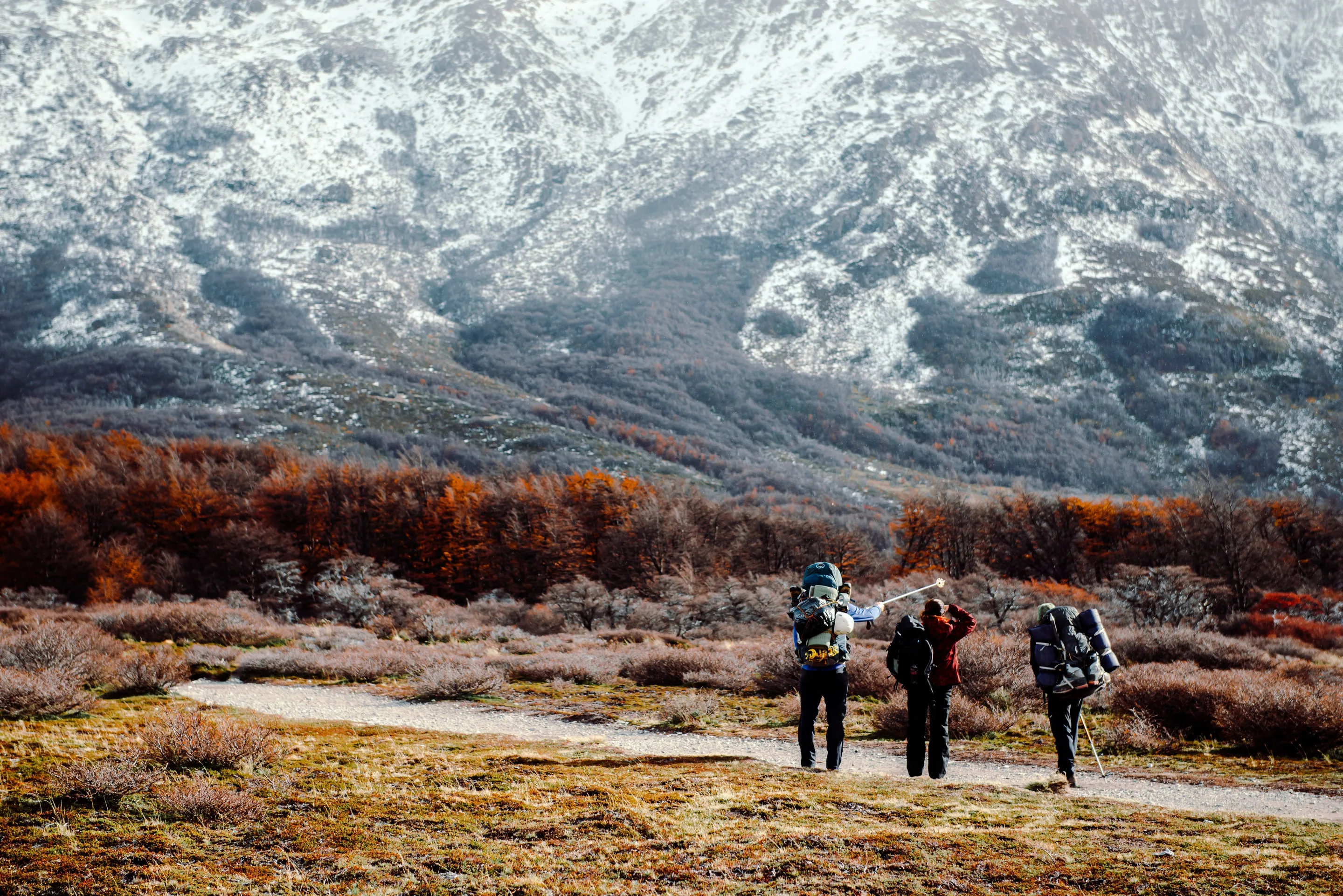 Three walkers approaching the mountains through autumn country