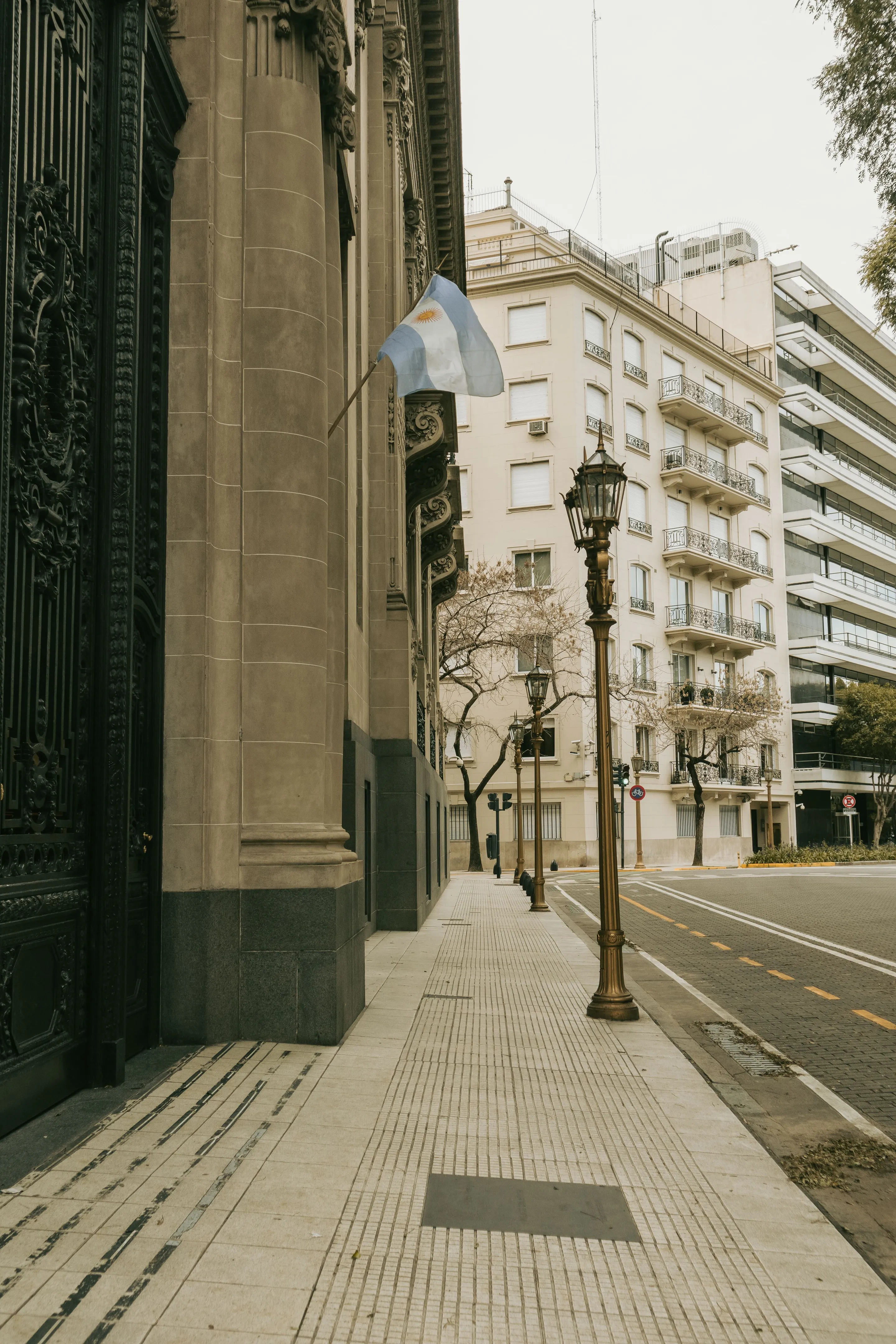 An empty sidewalk beside historic buildings and an Argentine flag in Buenos Aires