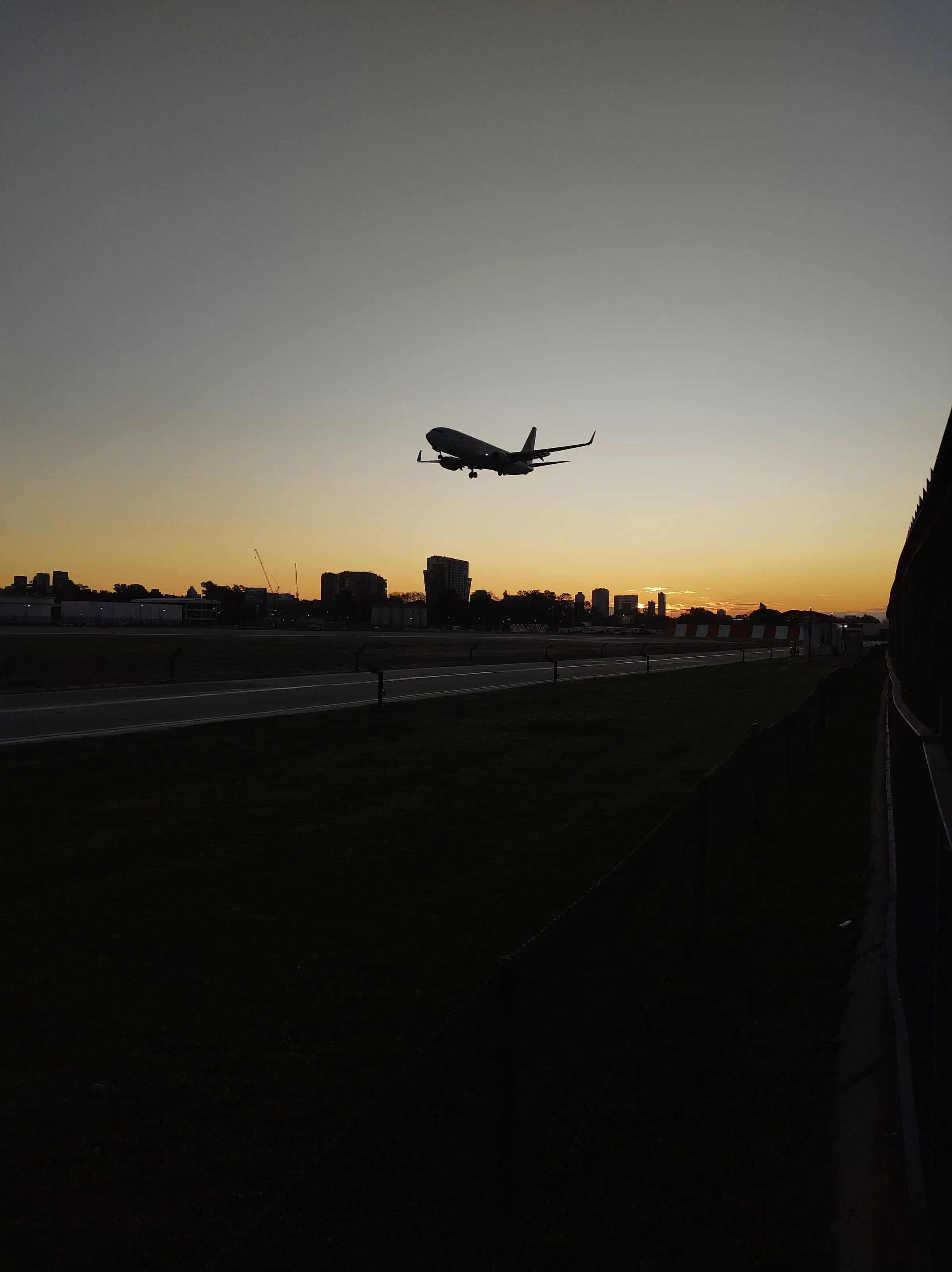 An aircraft silhouetted above a Buenos Aires runway at sunset.