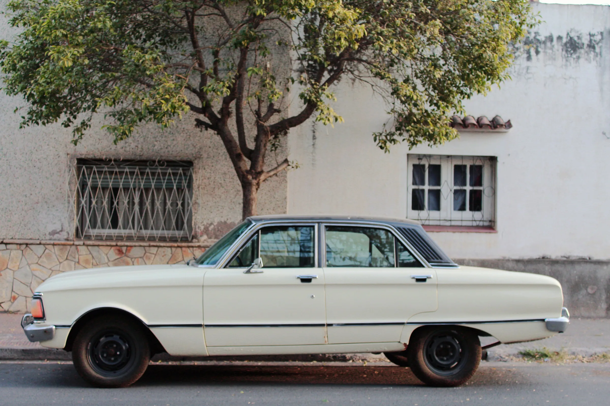 A vintage white car beside an old wall on a quiet Salta street.
