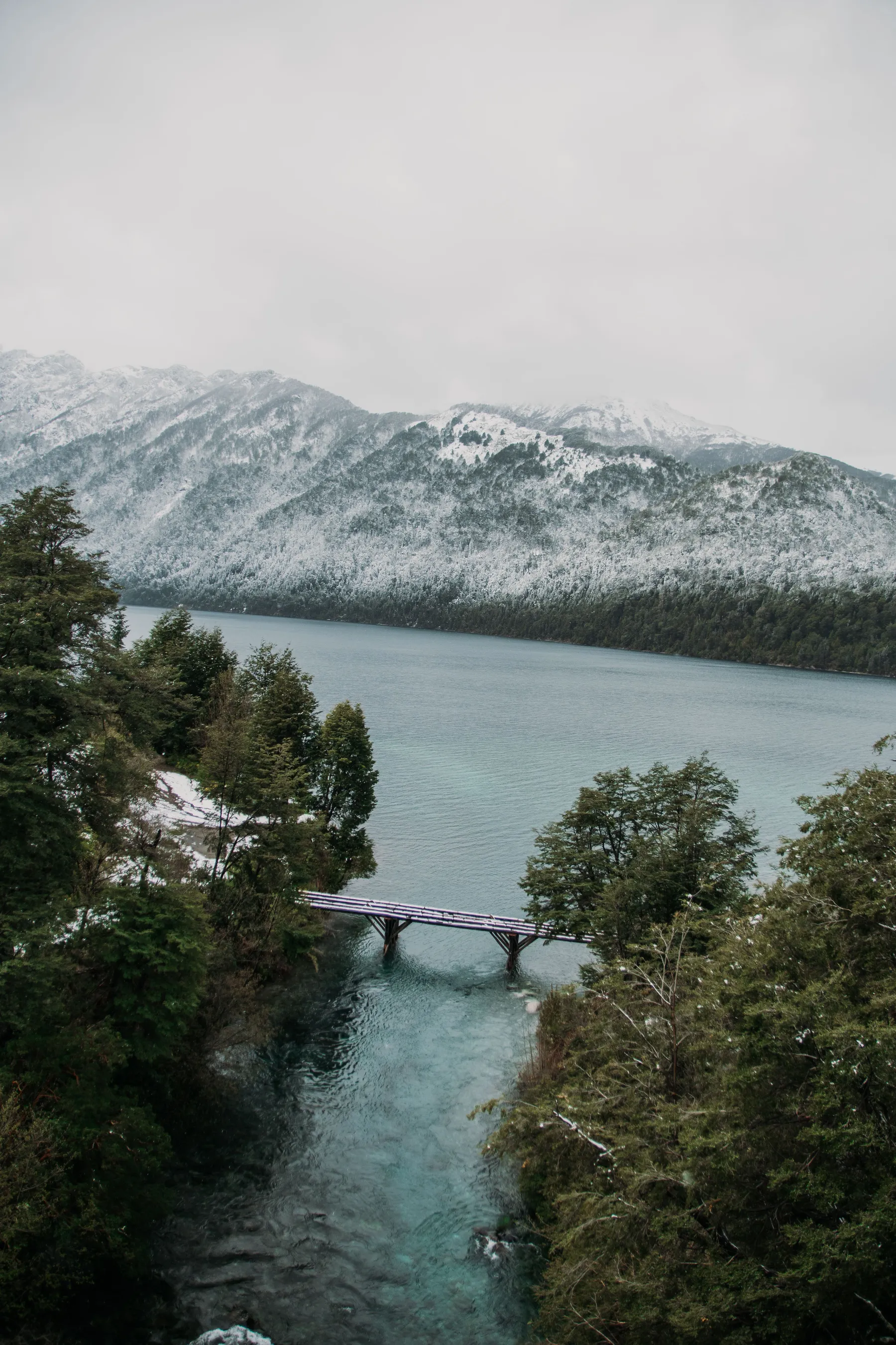 Bridge and clear water beneath snowy mountains at Correntoso