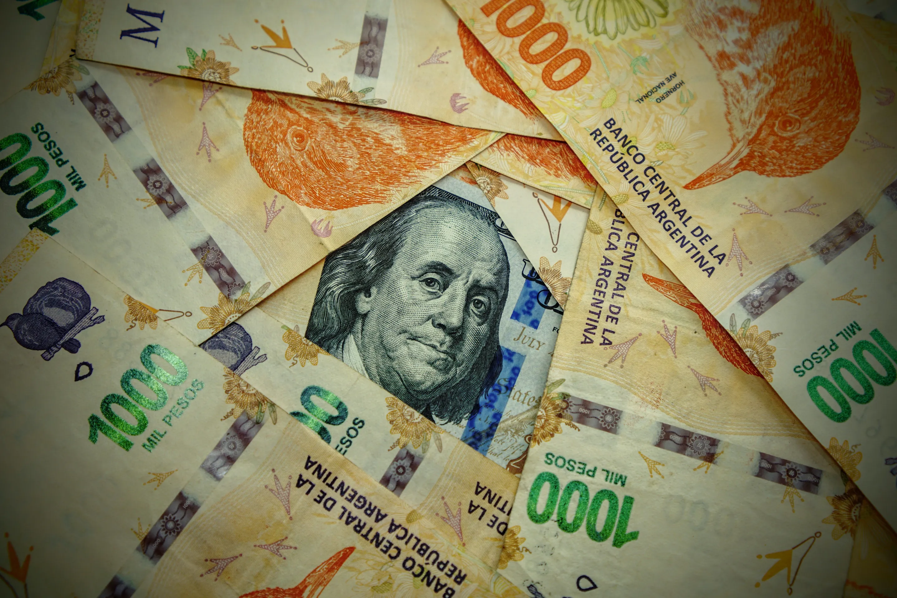 Argentine peso banknotes beside a US dollar.