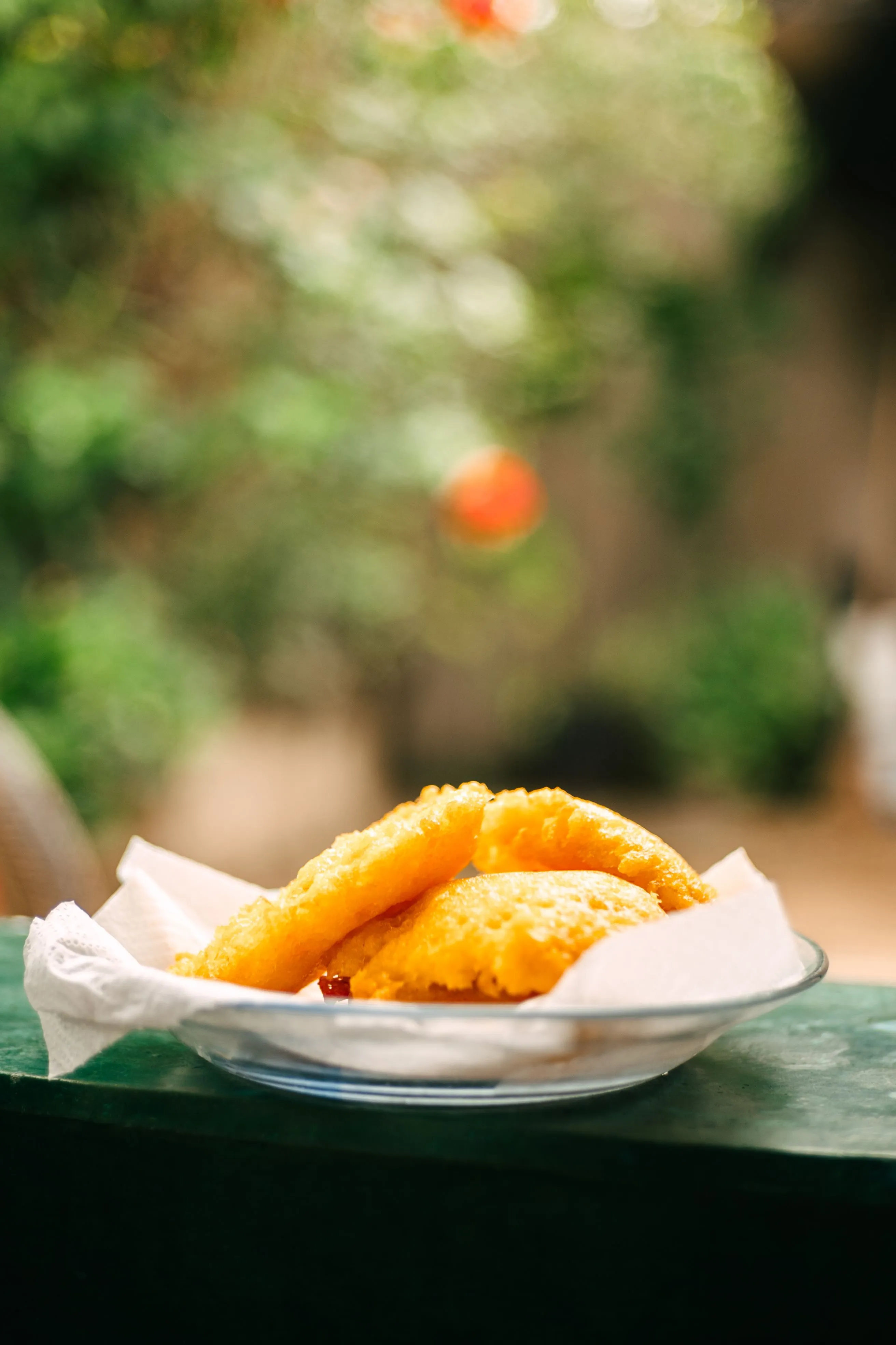 Golden empanadas on a glass plate against a softly blurred garden