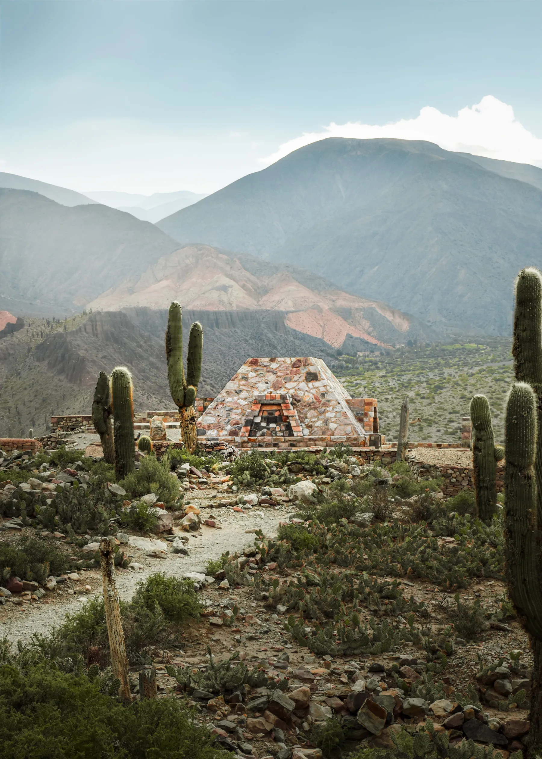 A stone monument among cacti and mountains at the Pucará de Tilcara