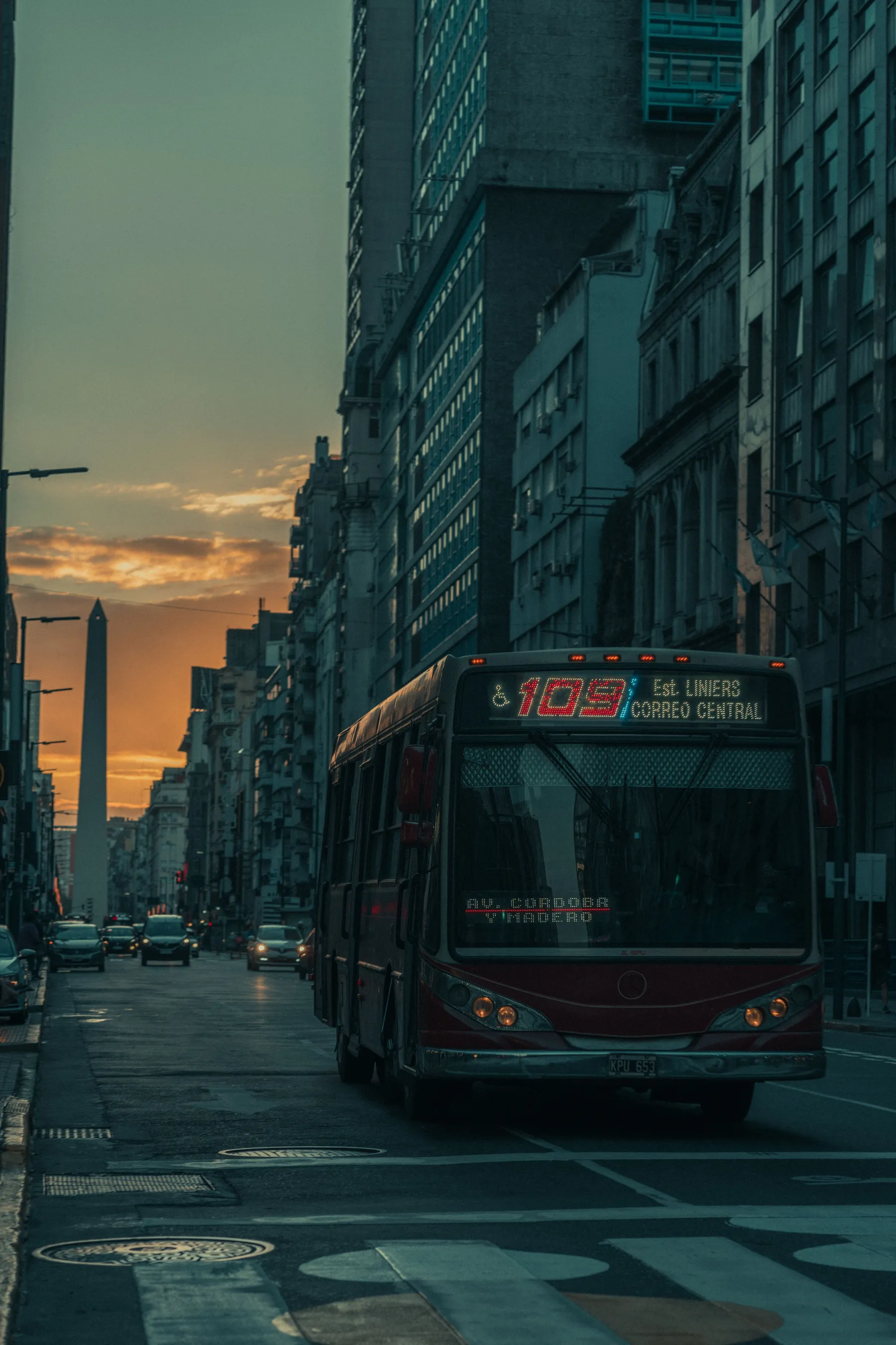 A red local bus on a Buenos Aires street at dusk.