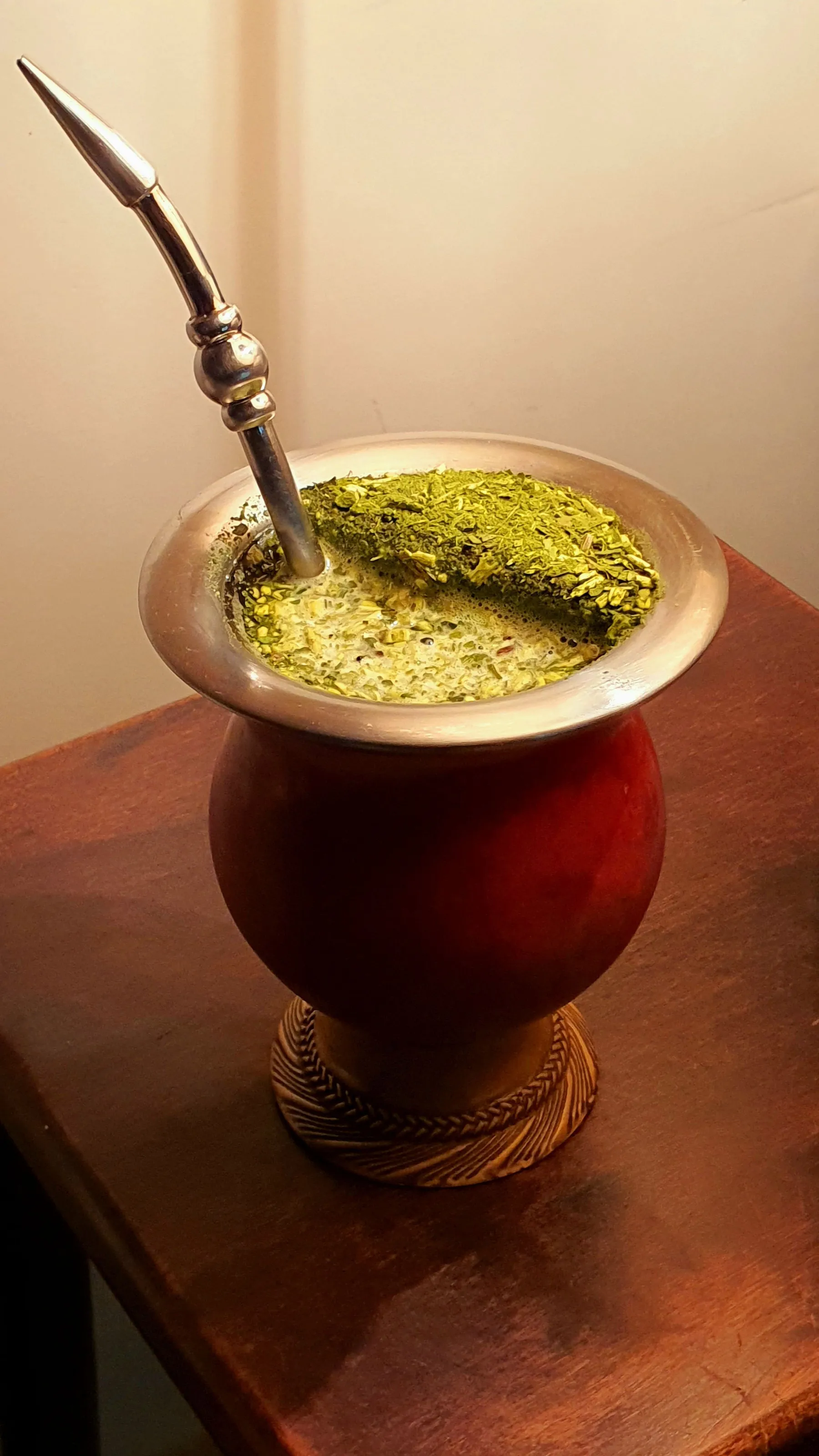 Close-up of yerba mate and a metal bombilla in a gourd on wood