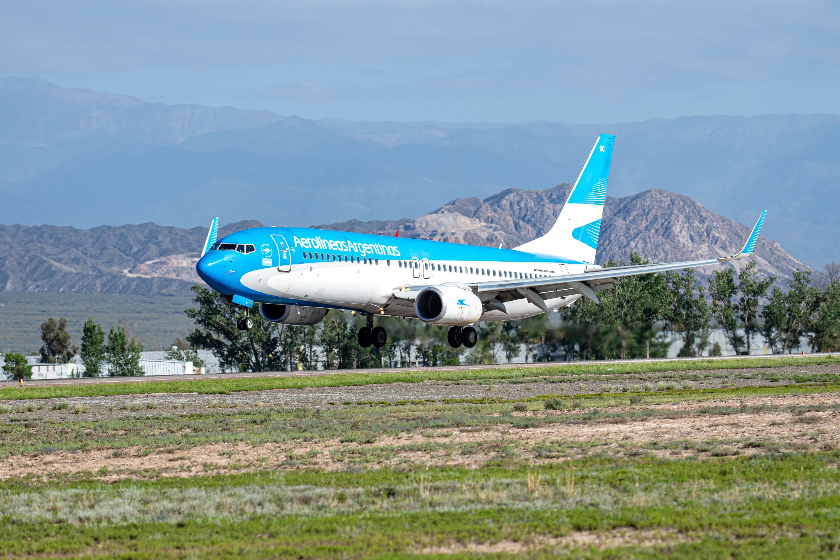 An Aerolíneas Argentinas aircraft approaching a mountain-framed runway.