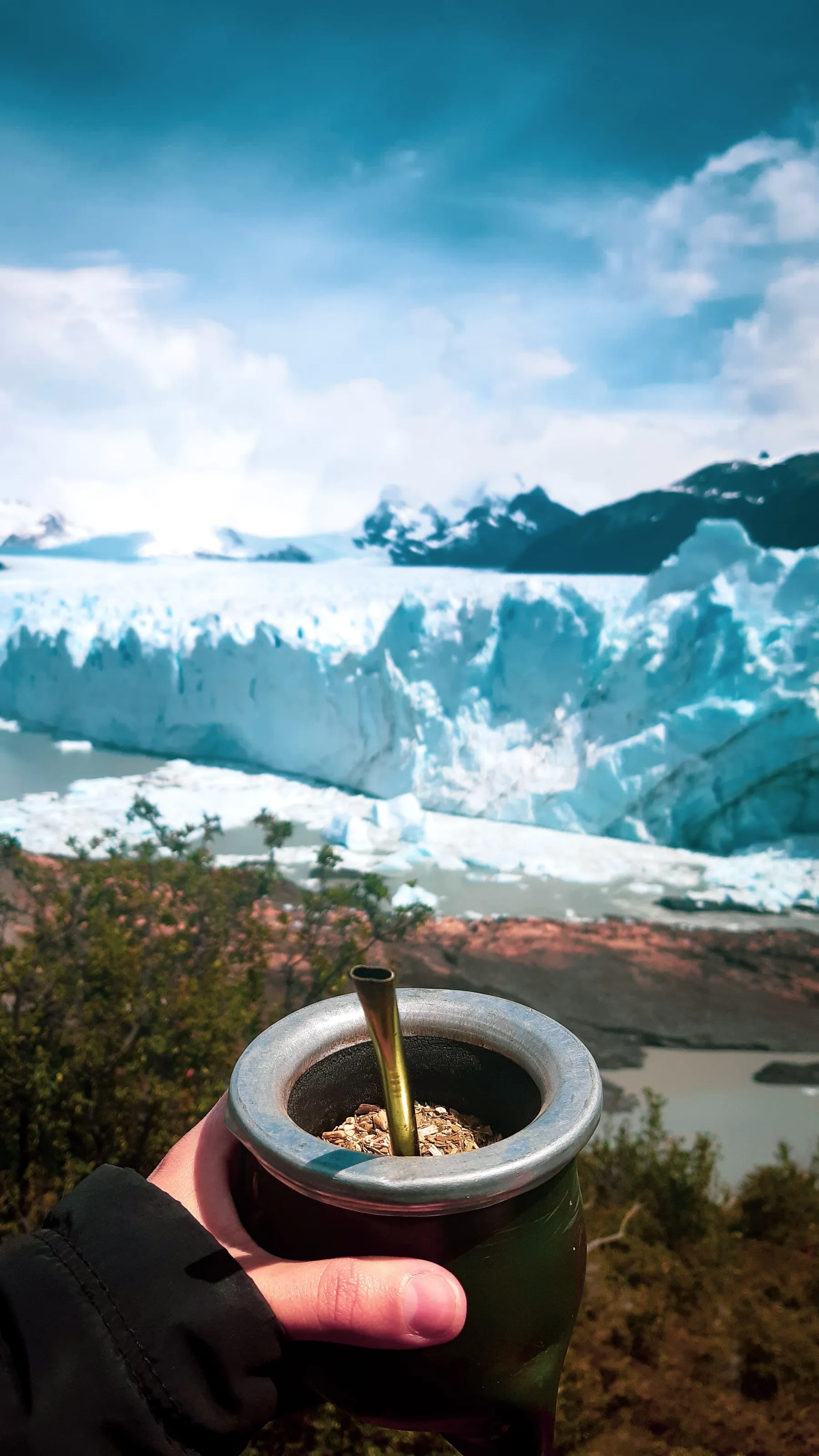 A hand holding mate close to the camera with the glacier behind