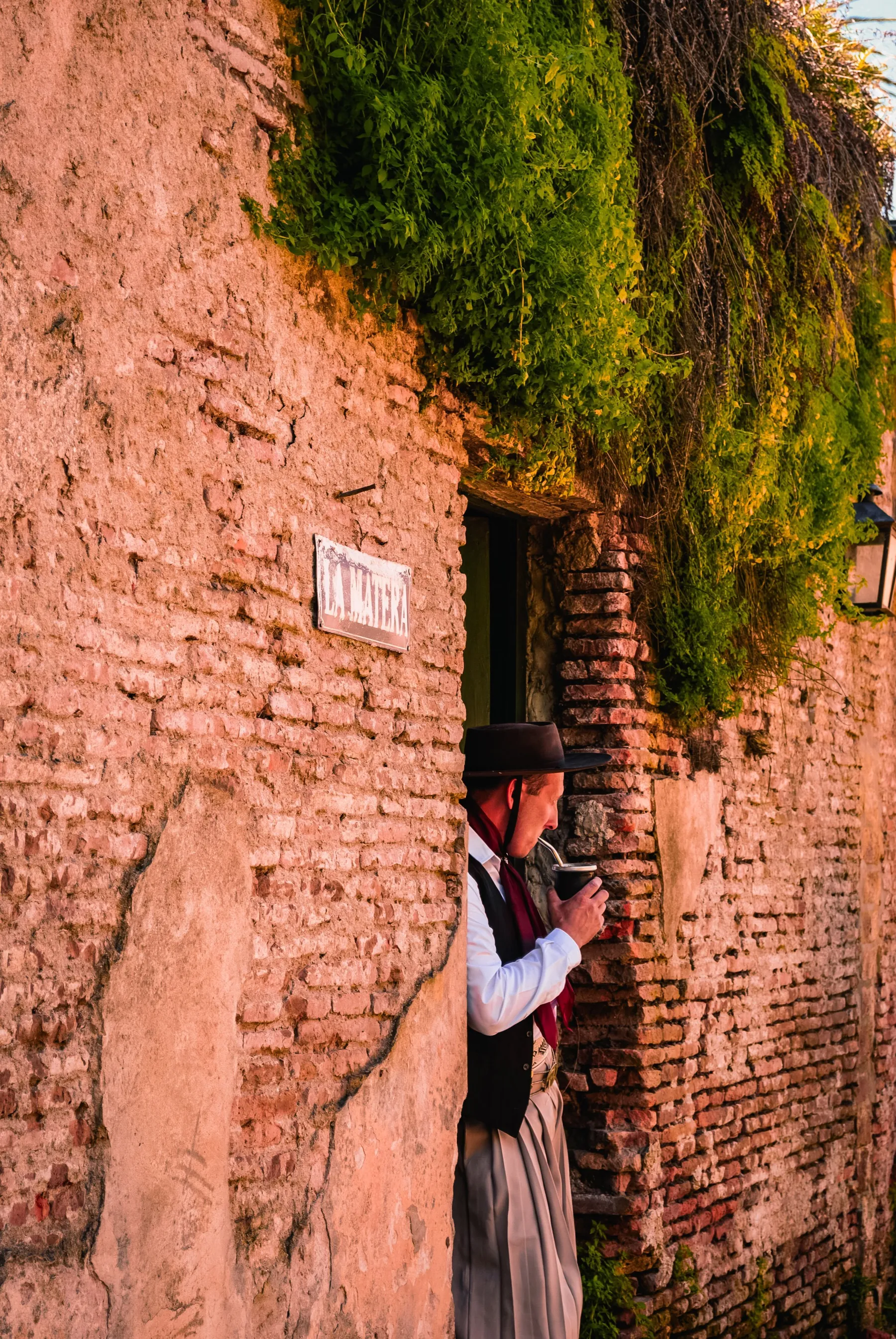 A person seated beside an old brick wall and doorway in Colonia del Sacramento