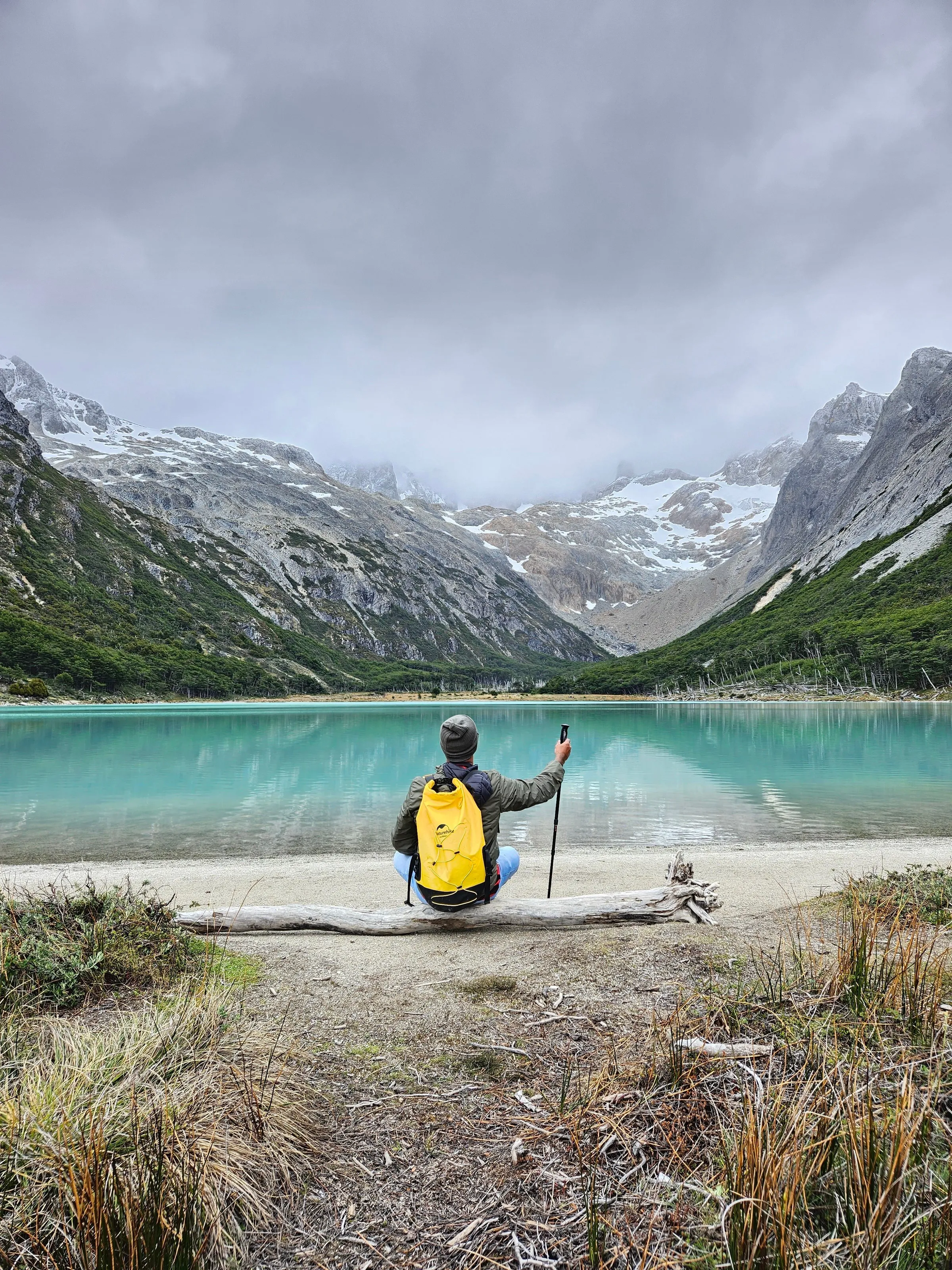 A hiker with a yellow backpack pauses above a mountain lake.