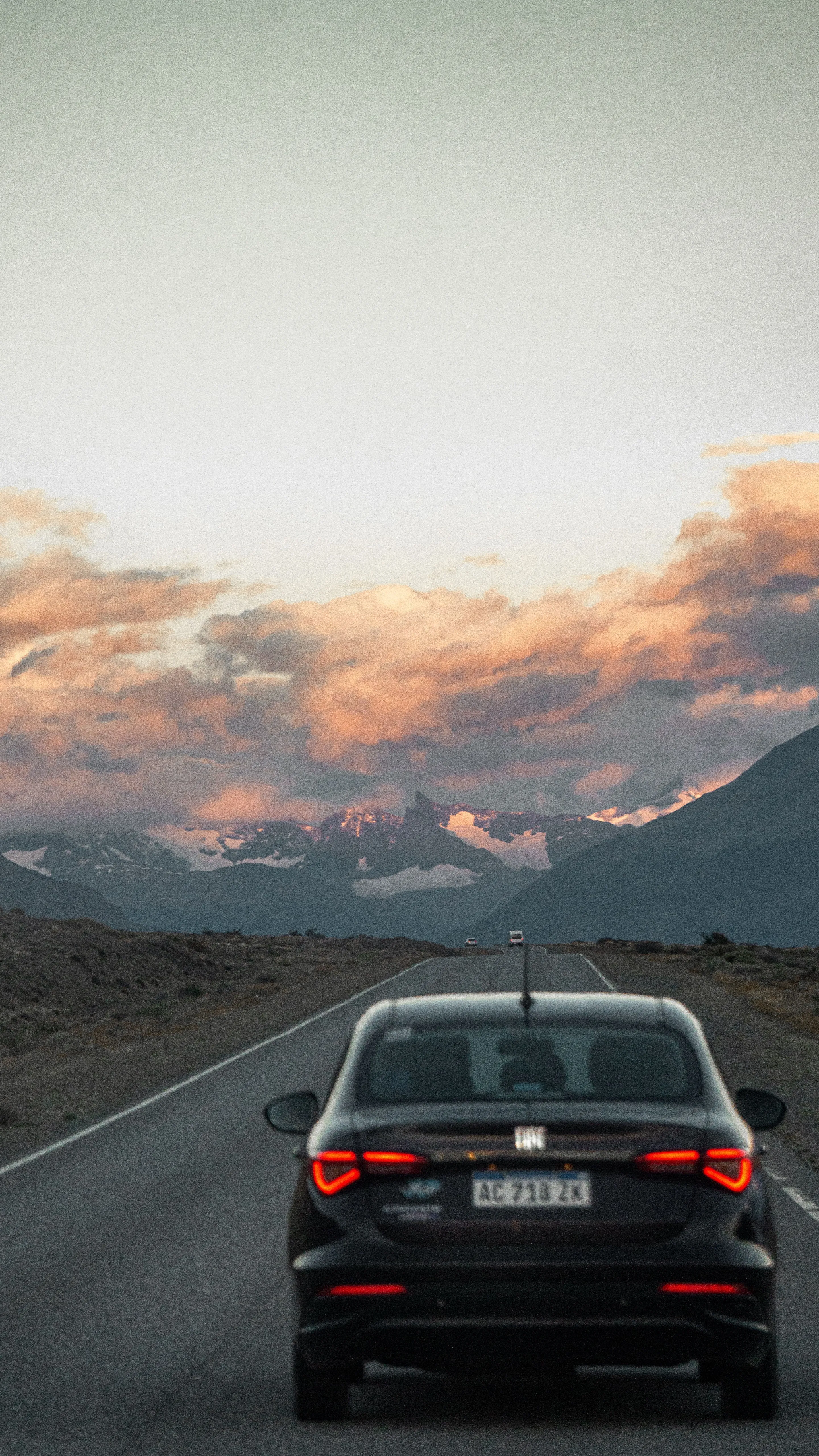 A car on a Patagonian road beneath dramatic sunset clouds.