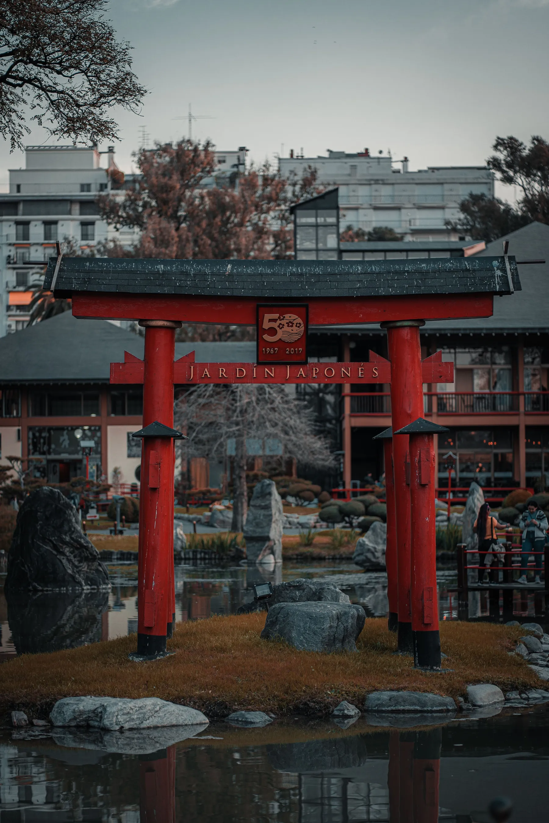 Red torii gate reflected in the Japanese Garden pond with the city beyond