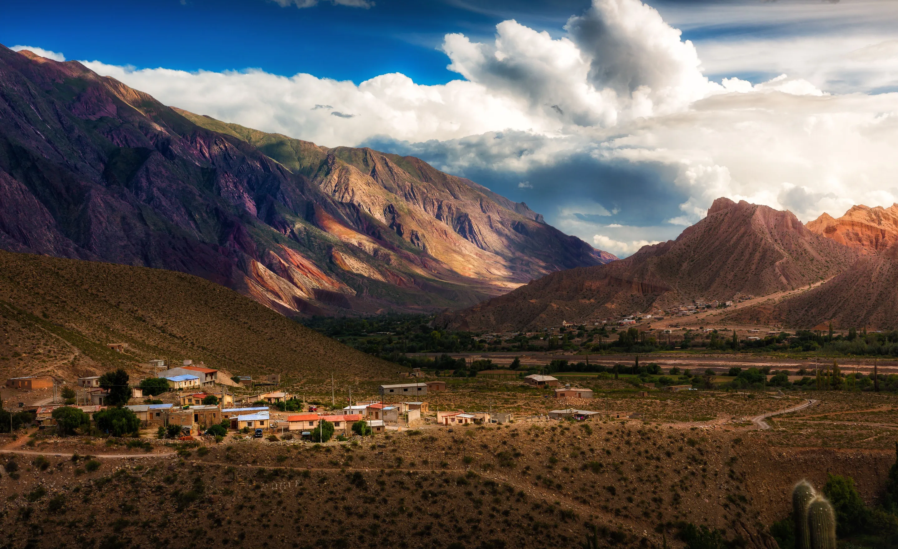 An Andean village beneath colourful mountains and dramatic clouds