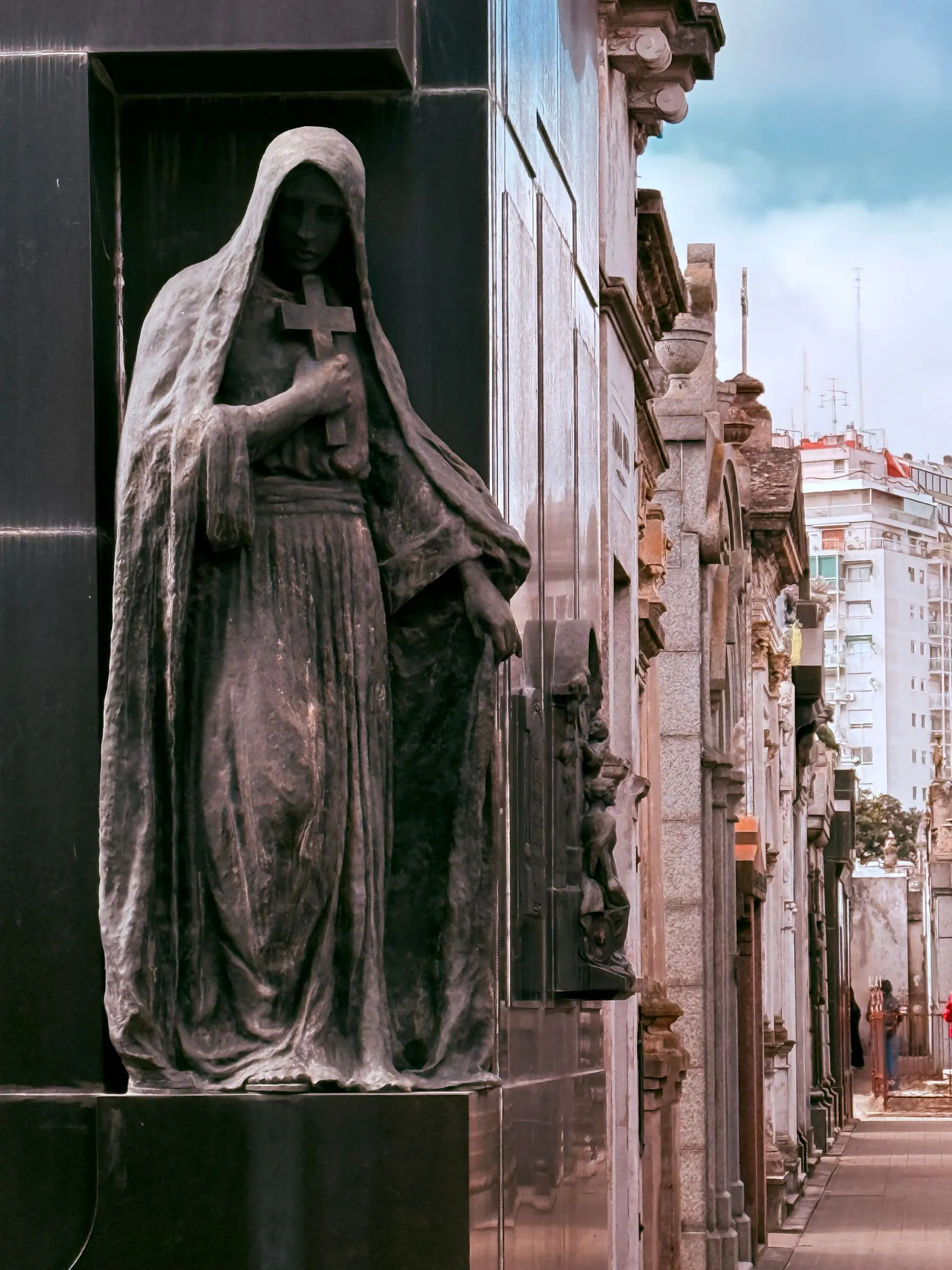 A weathered hooded figure beside the mausoleums of Recoleta Cemetery