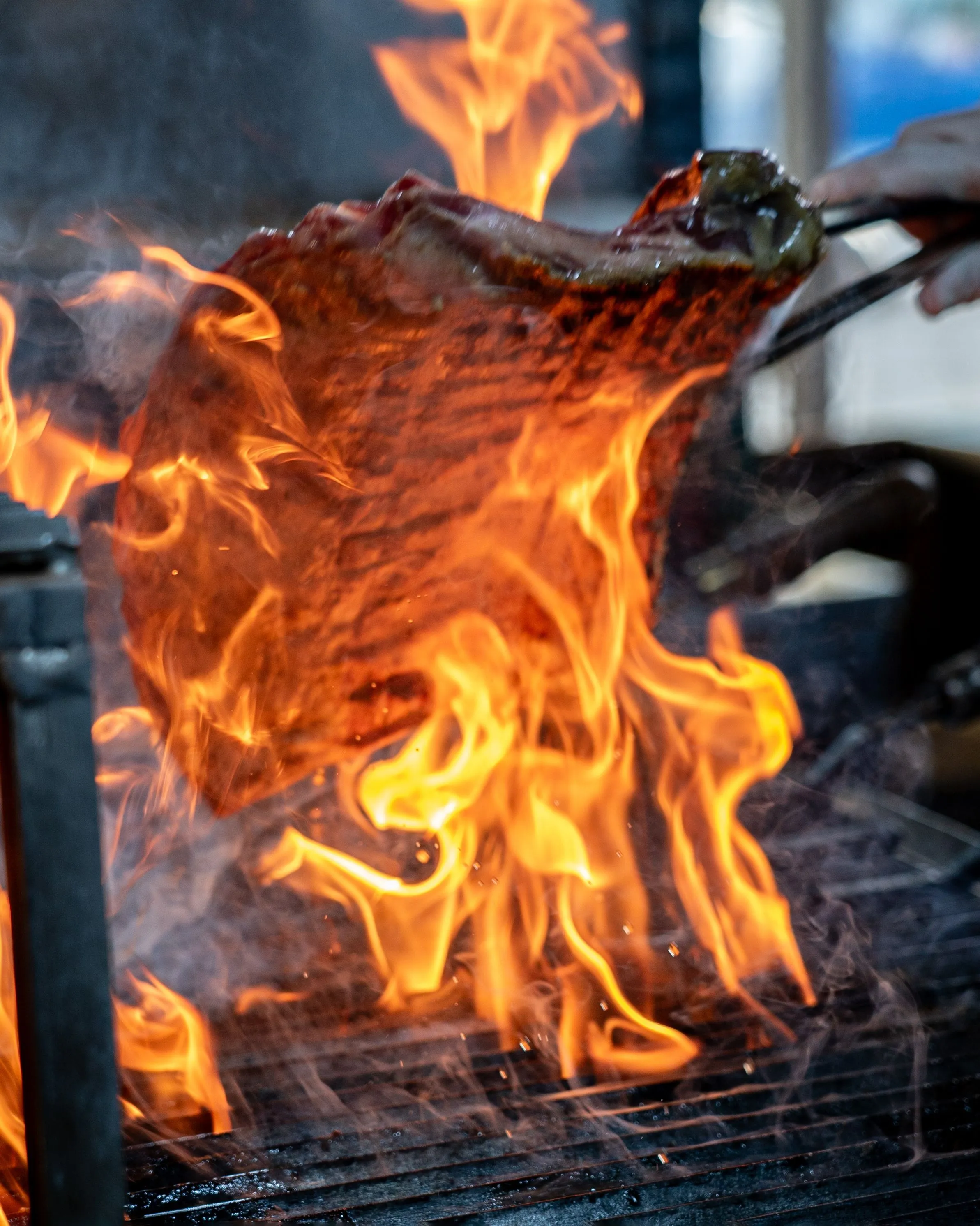 A steak searing over bright flames in a close view of the grill