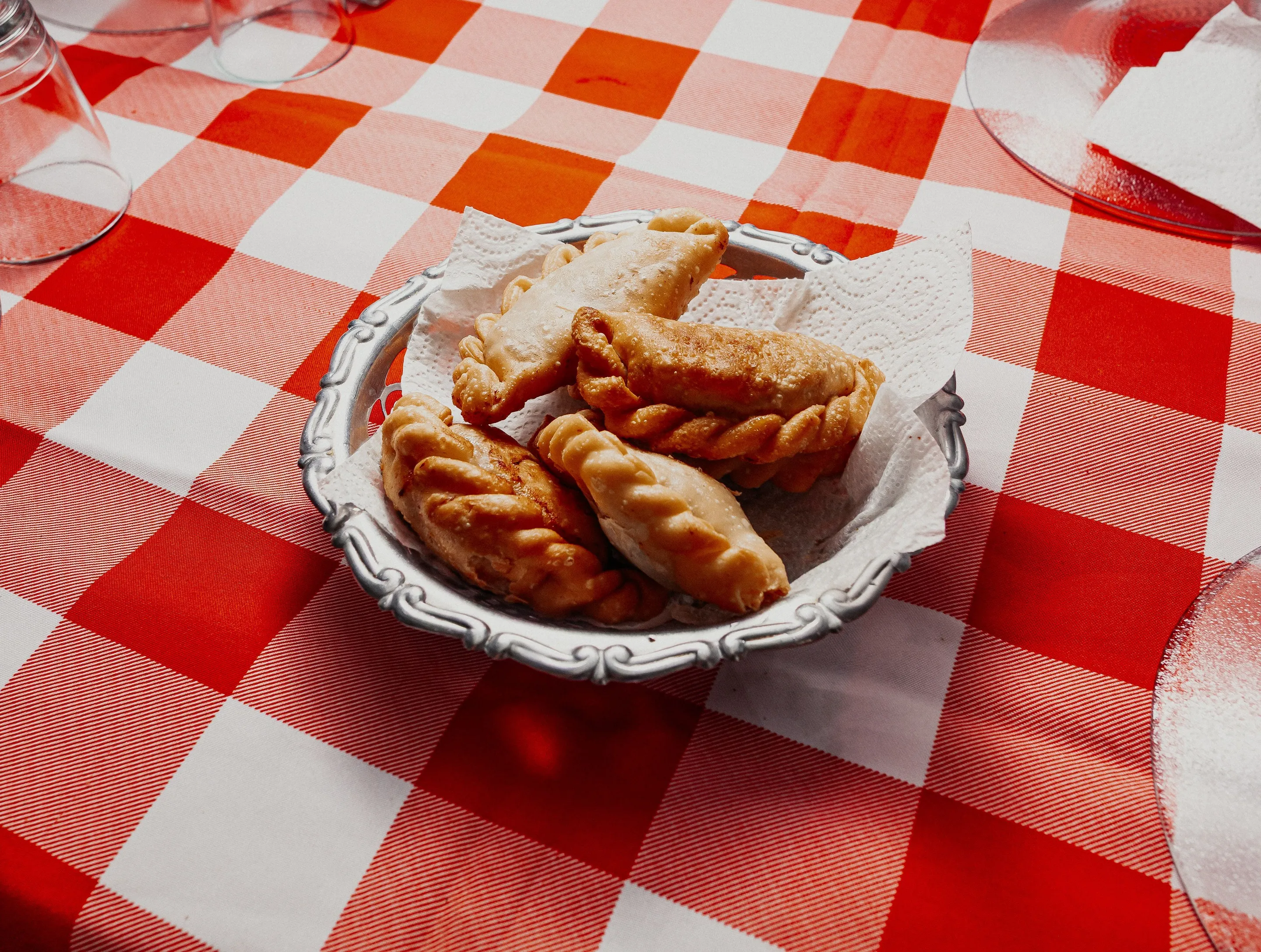 Golden Argentine empanadas on a red checked tablecloth.