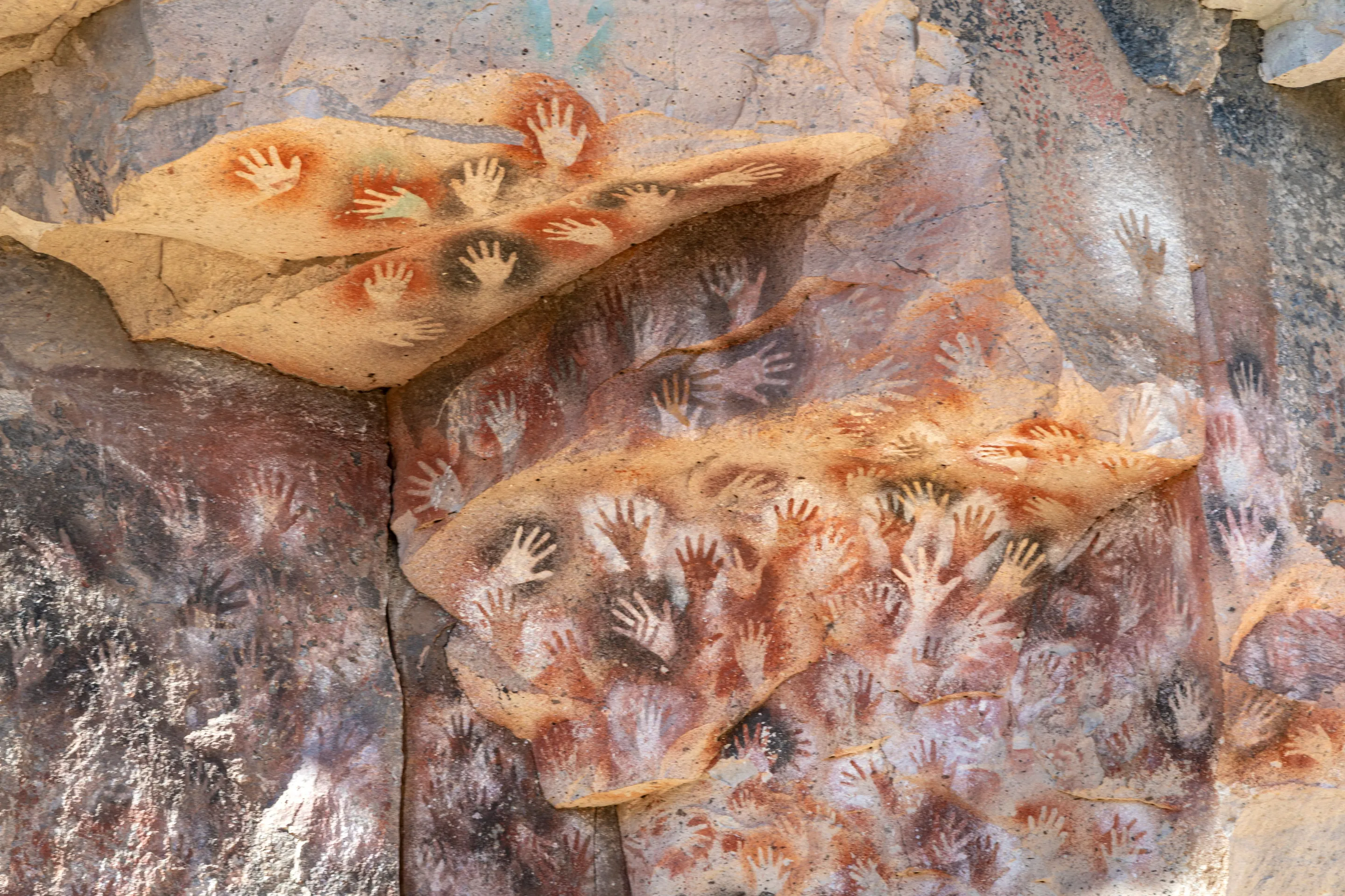 Ancient hand stencils across a painted rock wall