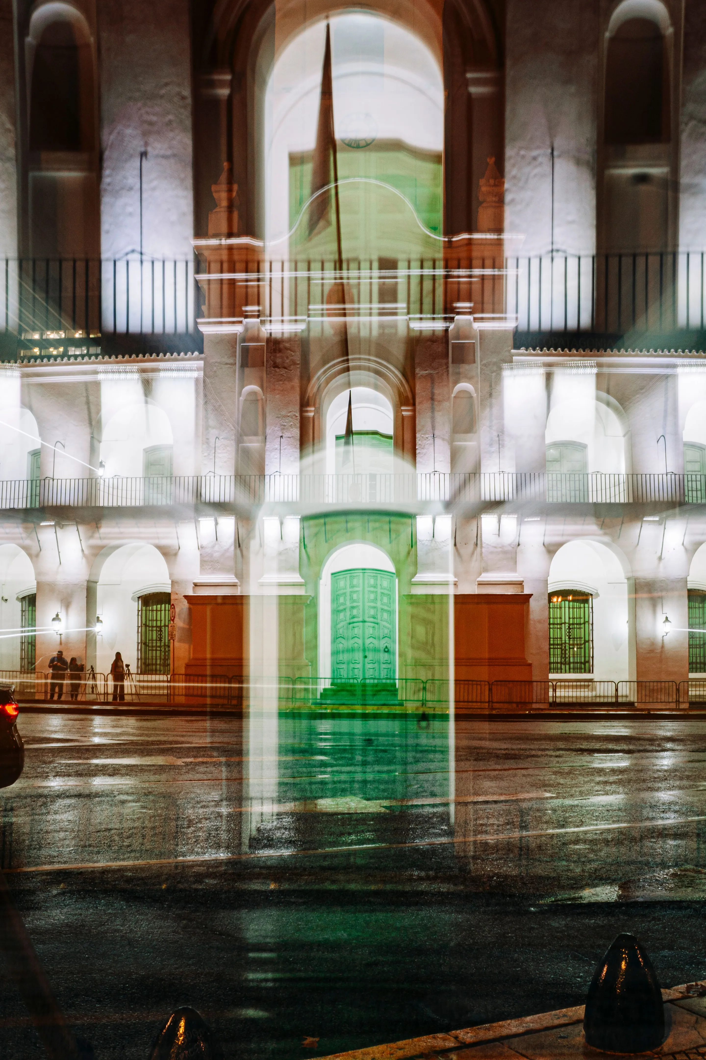 Illuminated Cabildo arches reflected on wet paving at night
