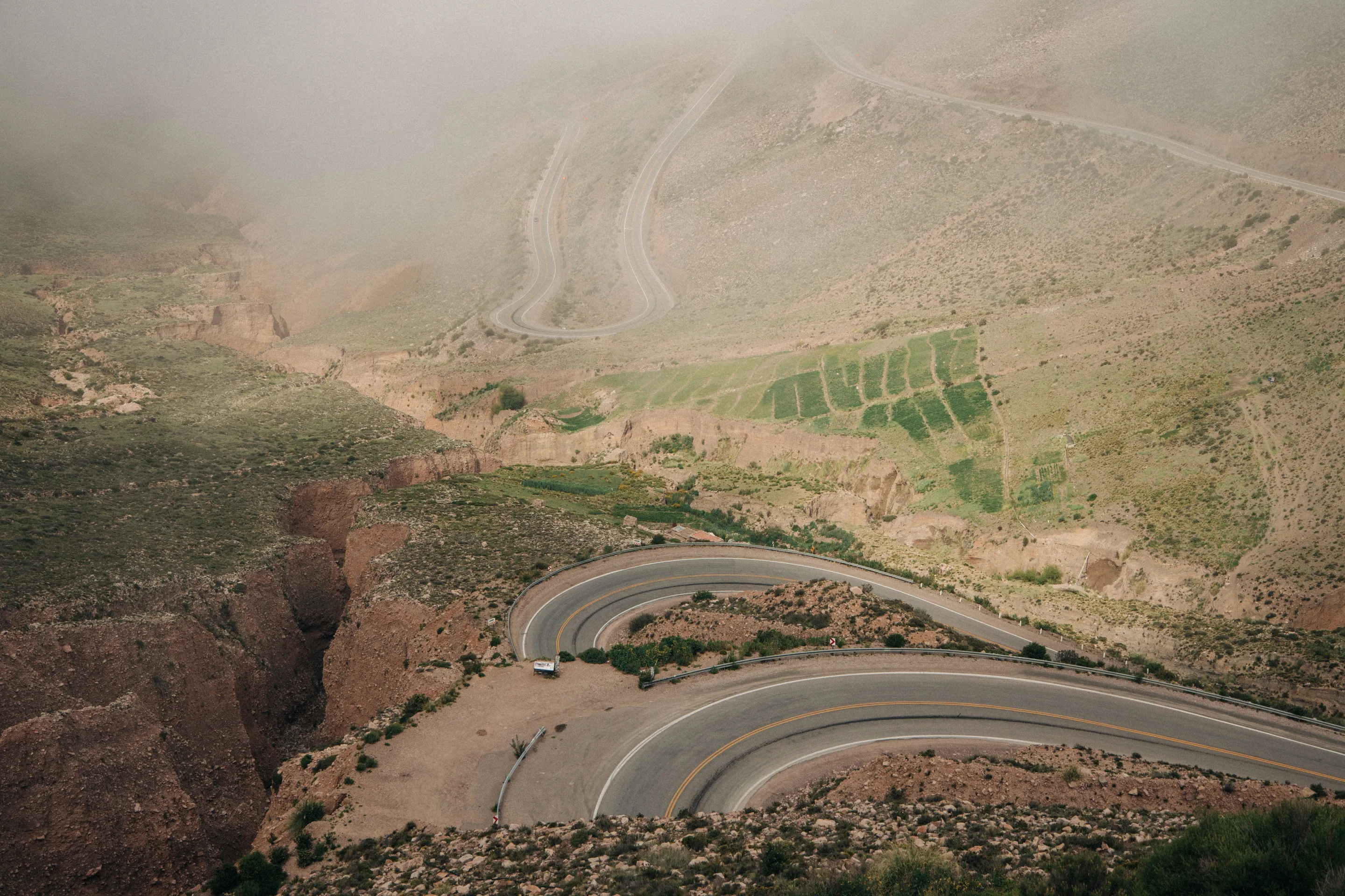 A mountain road winding between green and ochre ridges beneath low mist