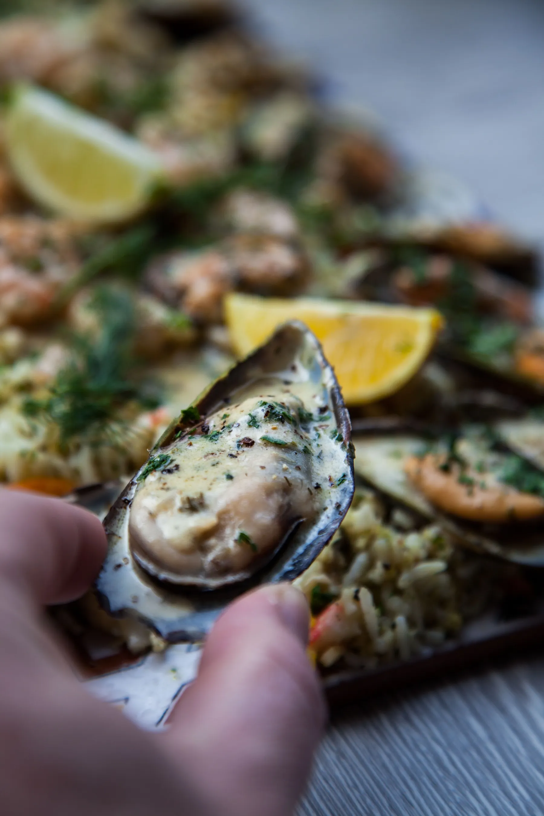 A hand lifting a mussel from a plate with sauce and herbs