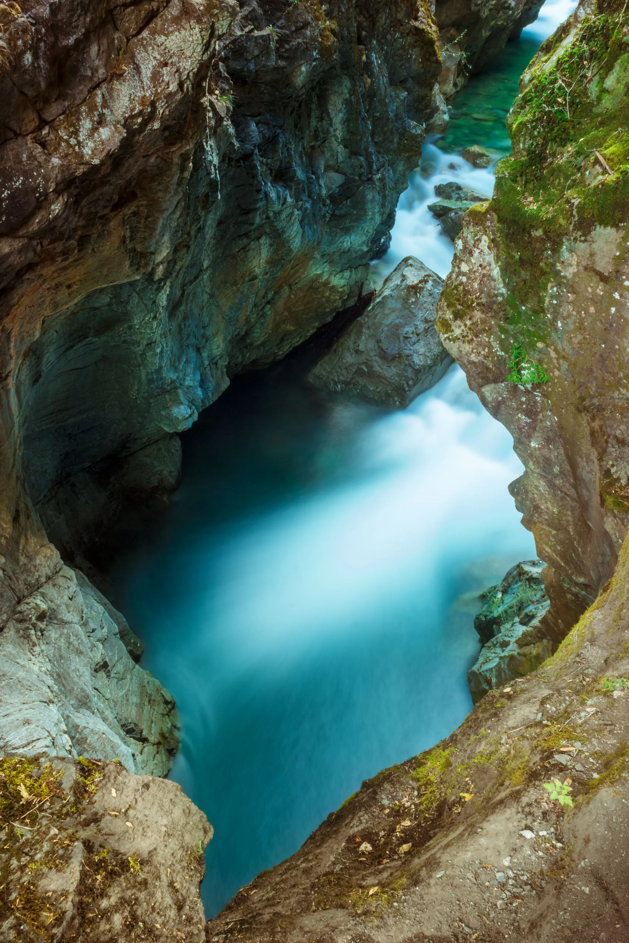 Clear blue water flowing through a dark wooded gorge near El Bolsón