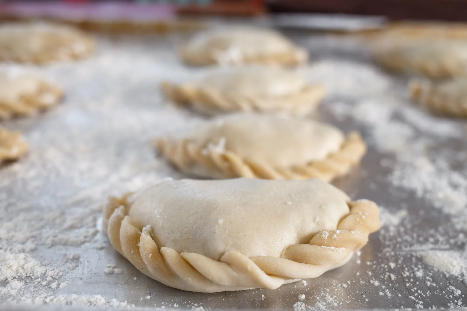 An uncooked empanada with a folded seal on a floured surface