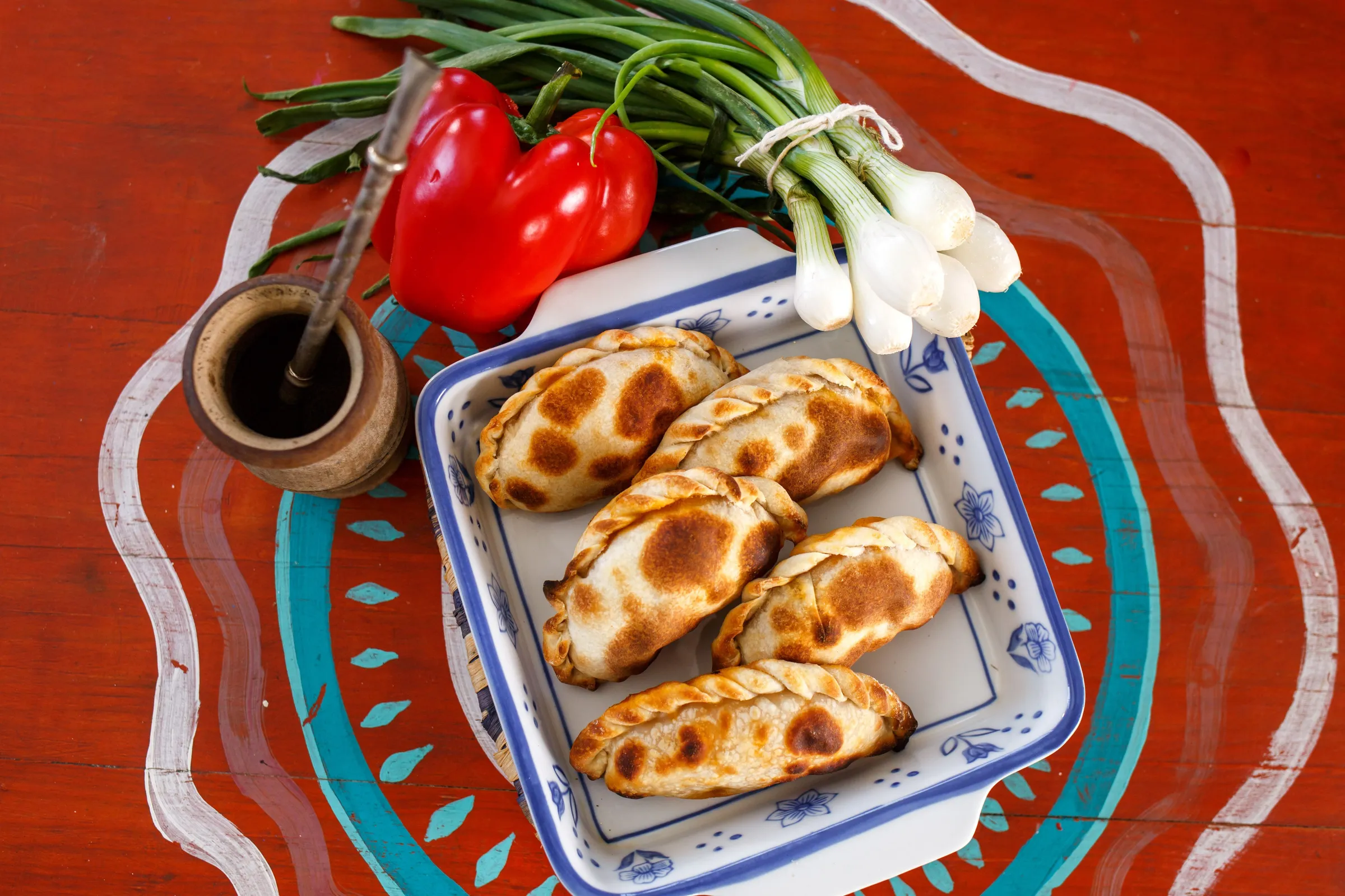 Argentine empanadas on a patterned plate beside fresh ingredients.