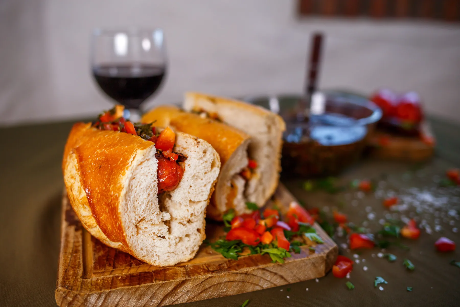 Close-up of a grilled chorizo sandwich with a glass of wine behind