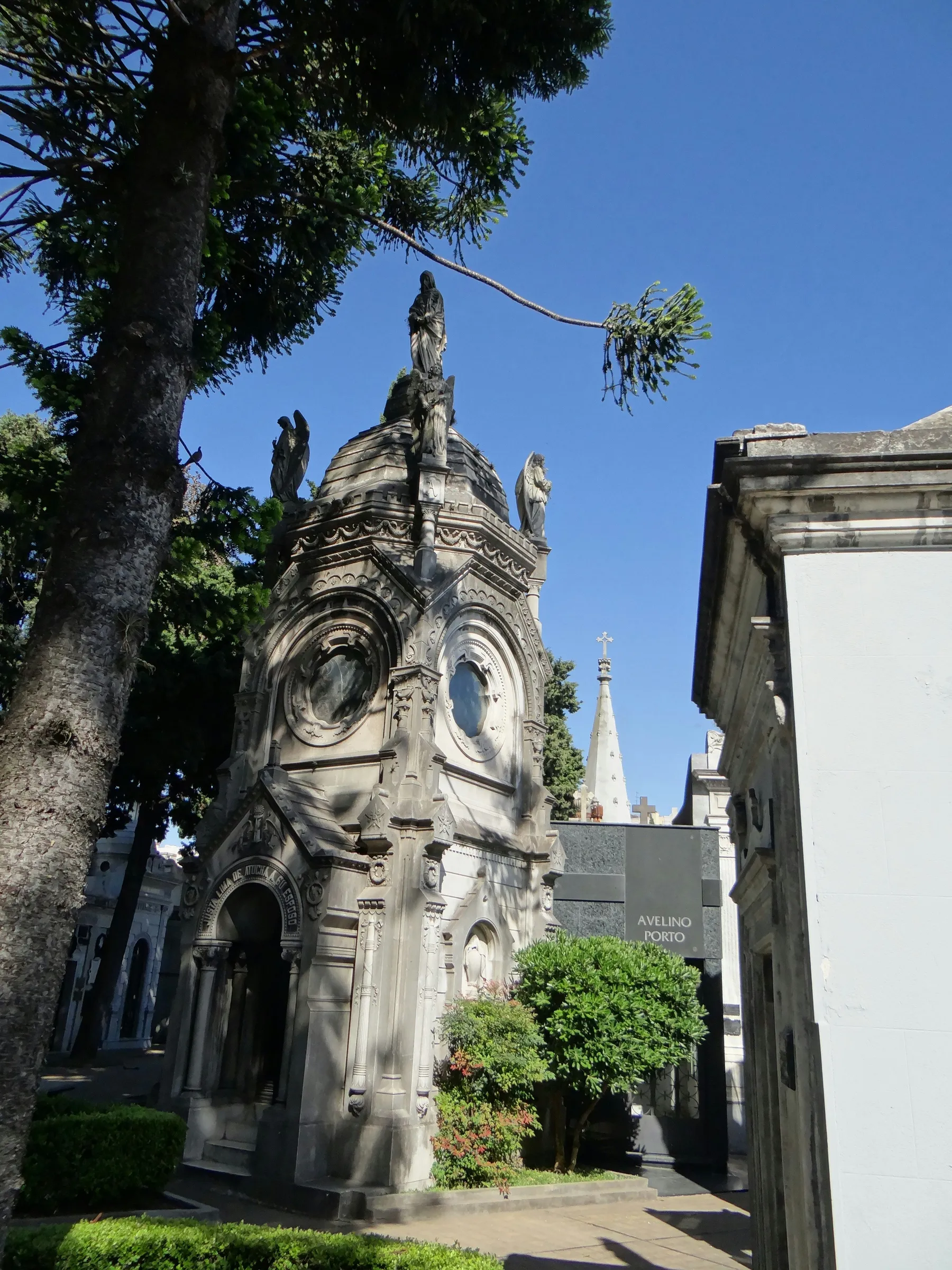 An ornate Recoleta mausoleum beneath a blue sky and shadowed trees