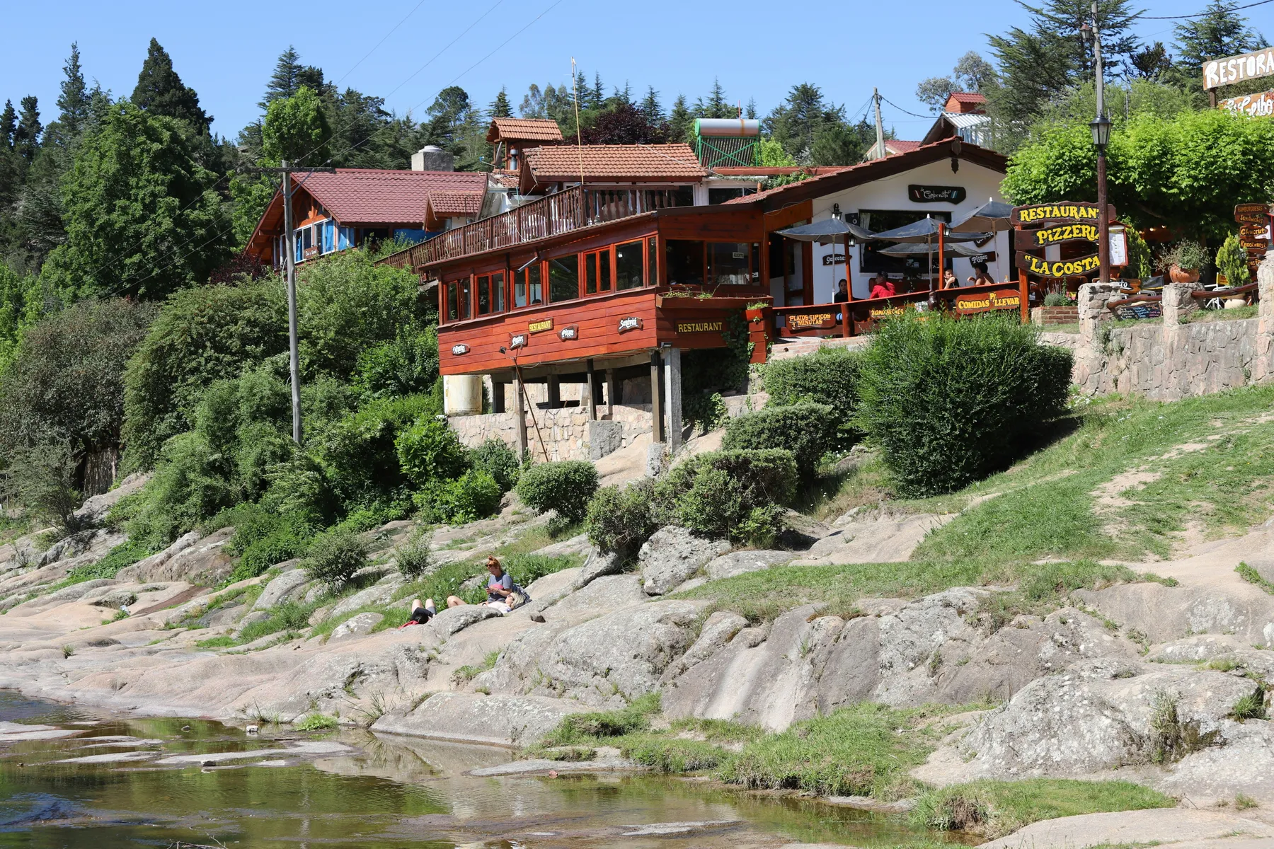 Riverside timber buildings beneath trees in La Cumbrecita
