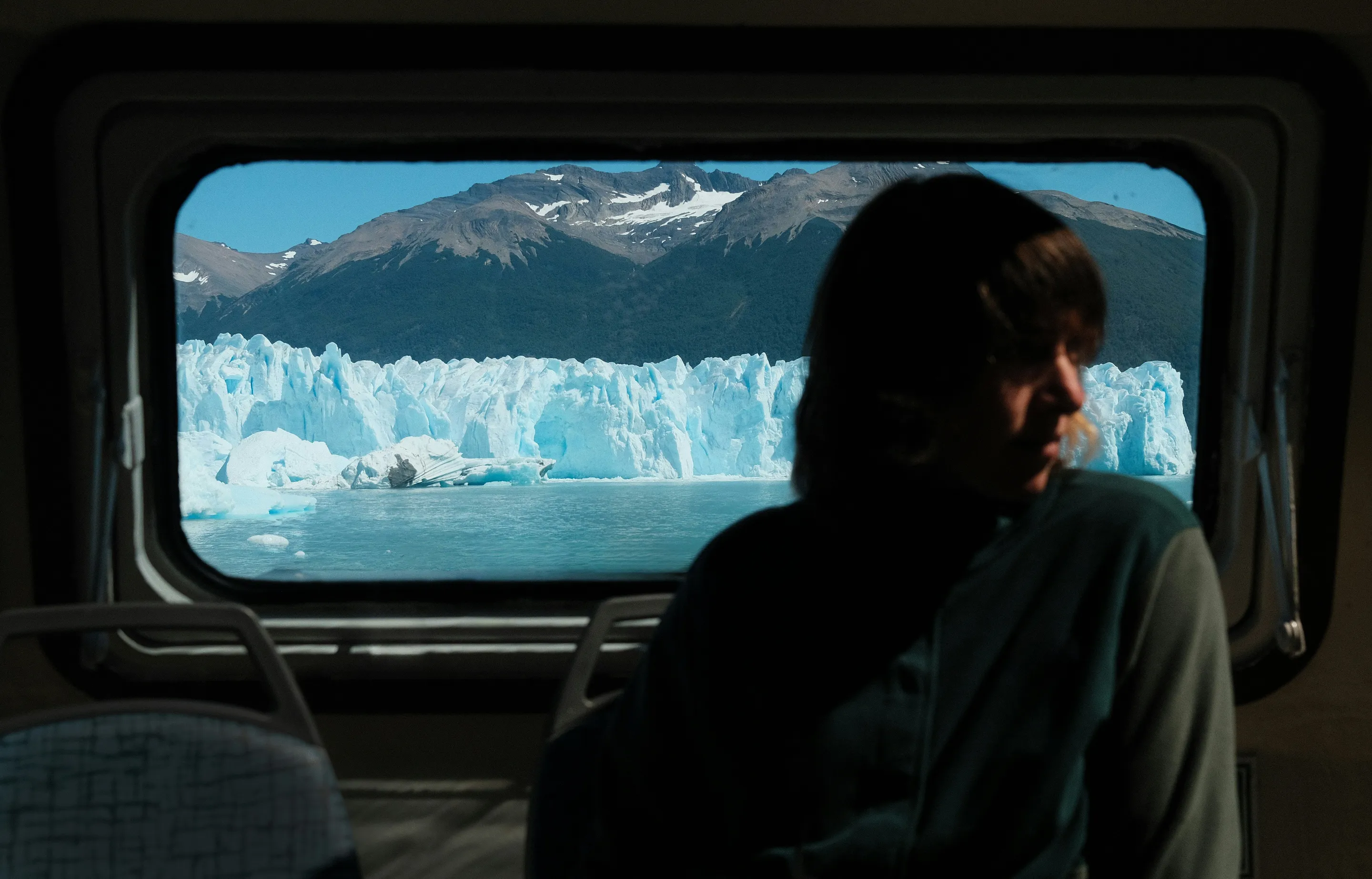 A traveller framed by a tour-bus window in front of Perito Moreno Glacier.