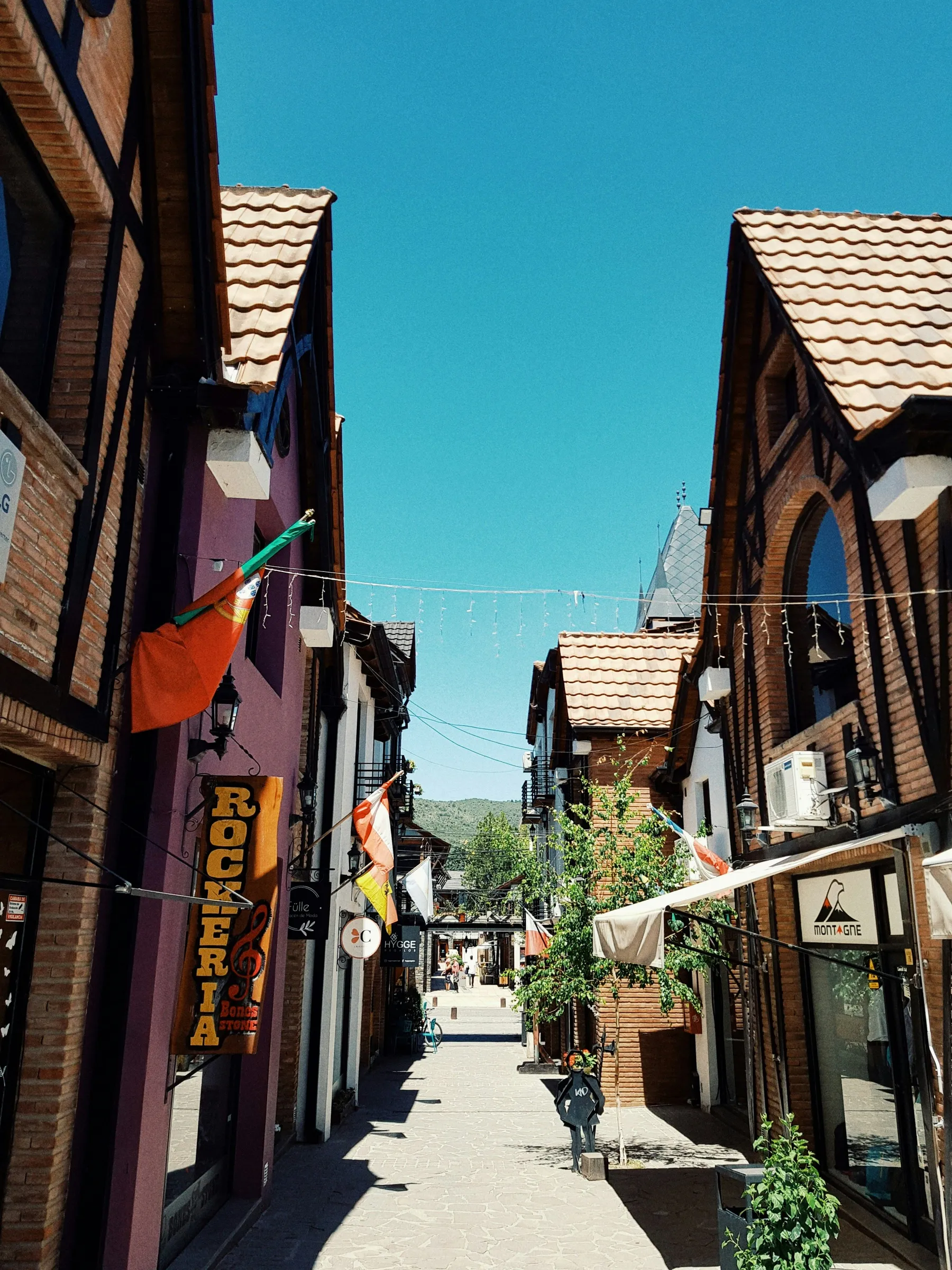 Timber-fronted buildings and flags along a Villa General Belgrano passage
