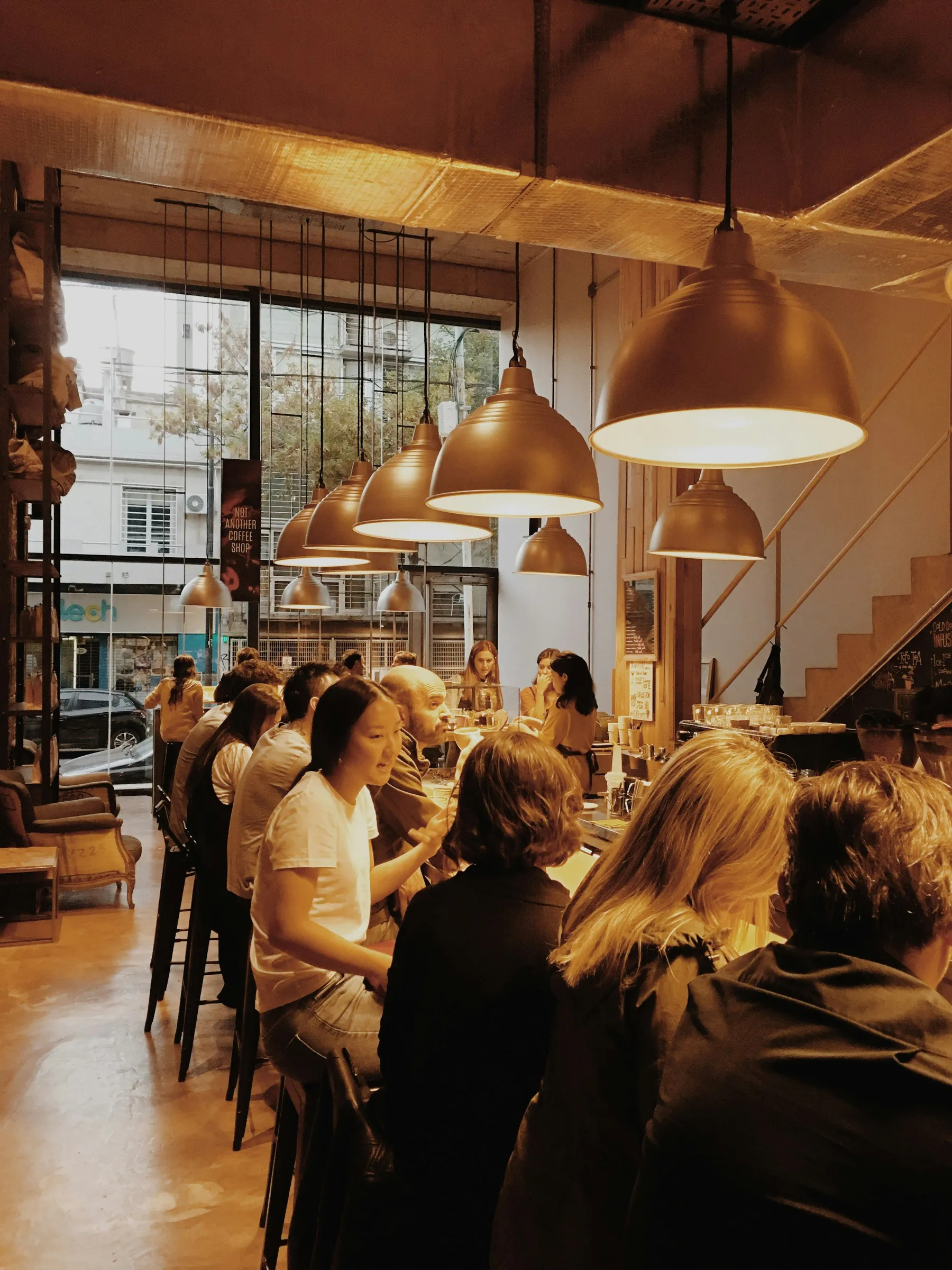People talking beneath warm pendant lights beside a Buenos Aires café window