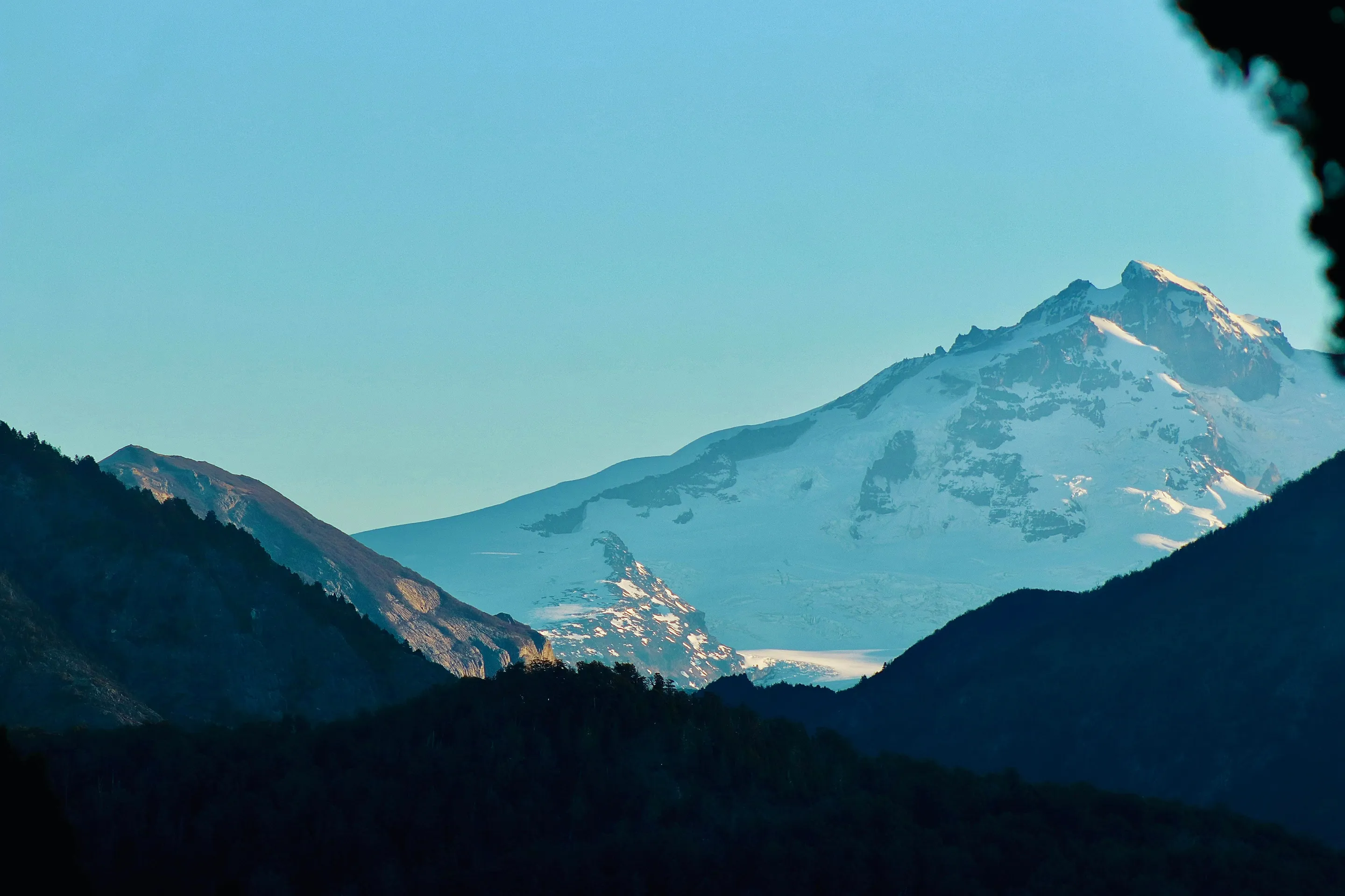 Snow-covered Tronador framed by dark mountain ridges beneath blue sky