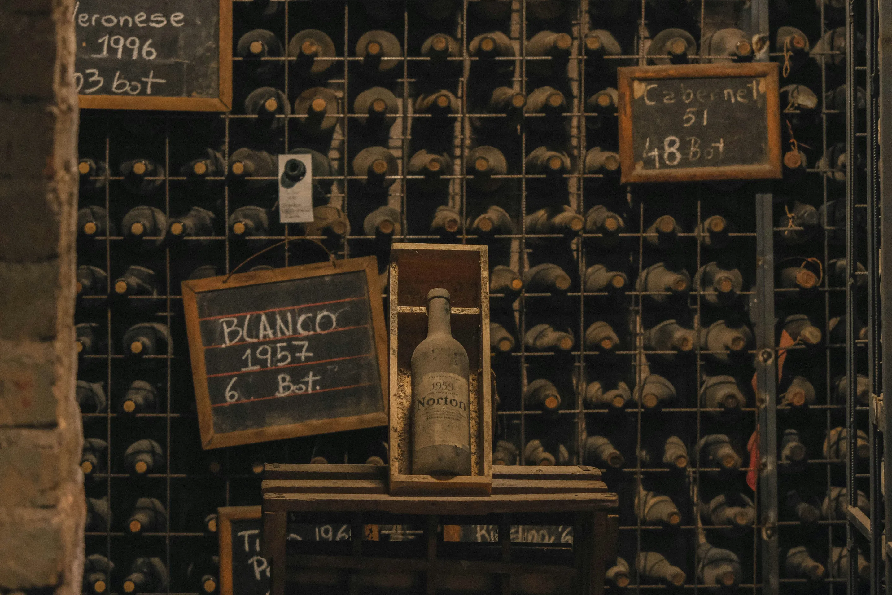 Wine bottles stored beside chalkboards in a cellar.