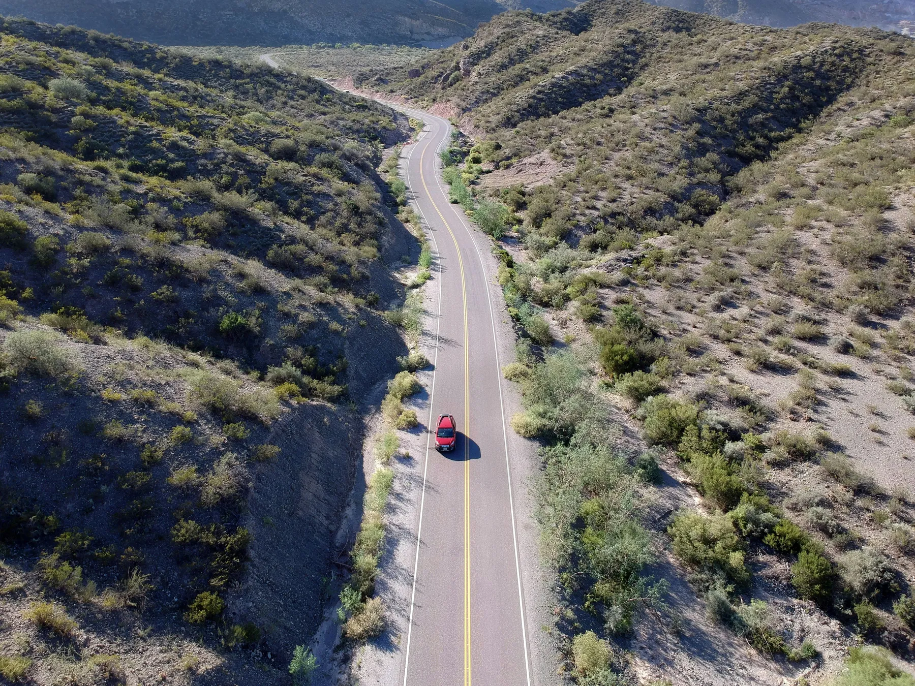 A small red car on a road through the arid landscape of Sarmiento