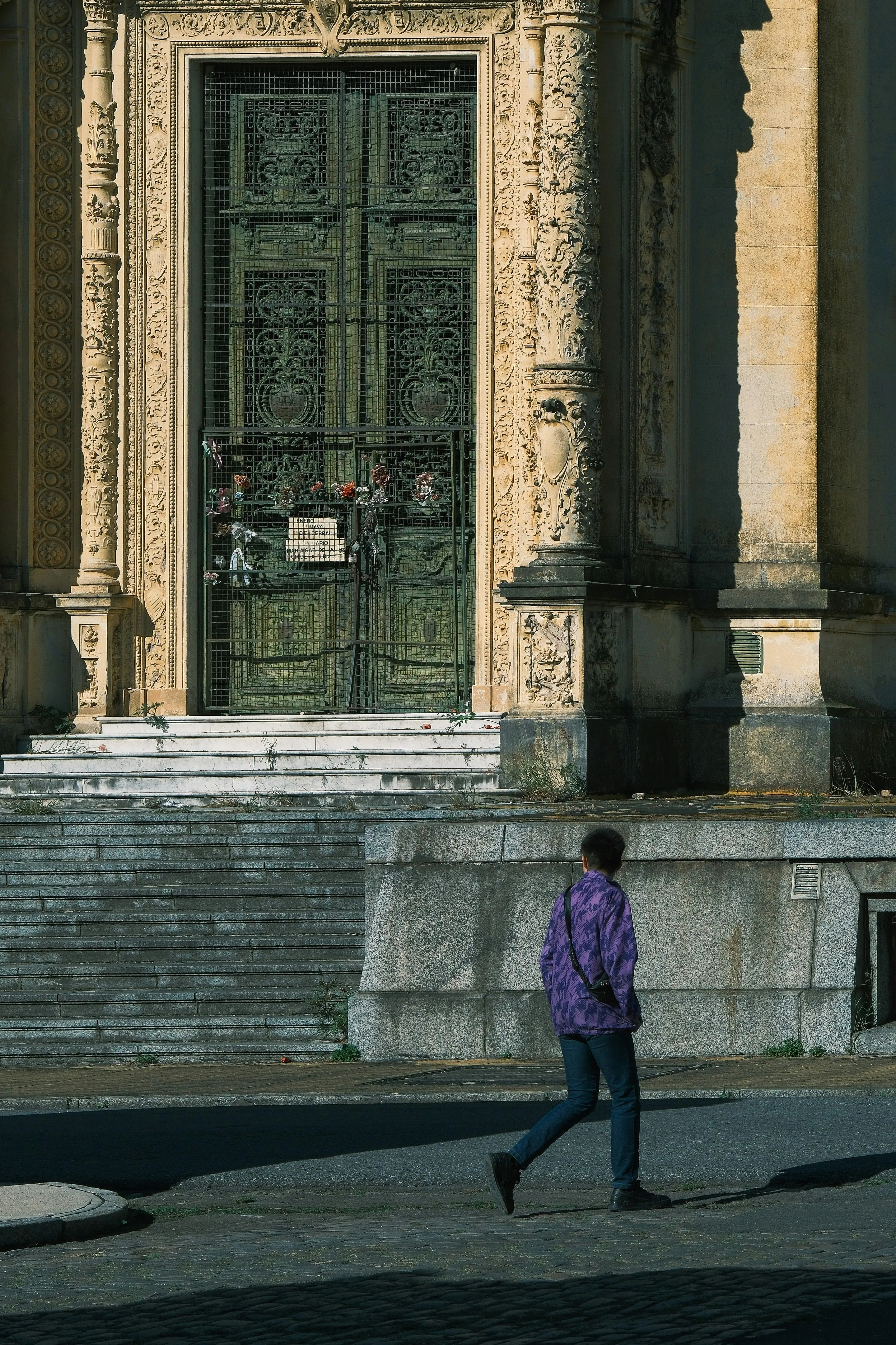 A person walking beneath an ornate mausoleum doorway in Chacarita Cemetery