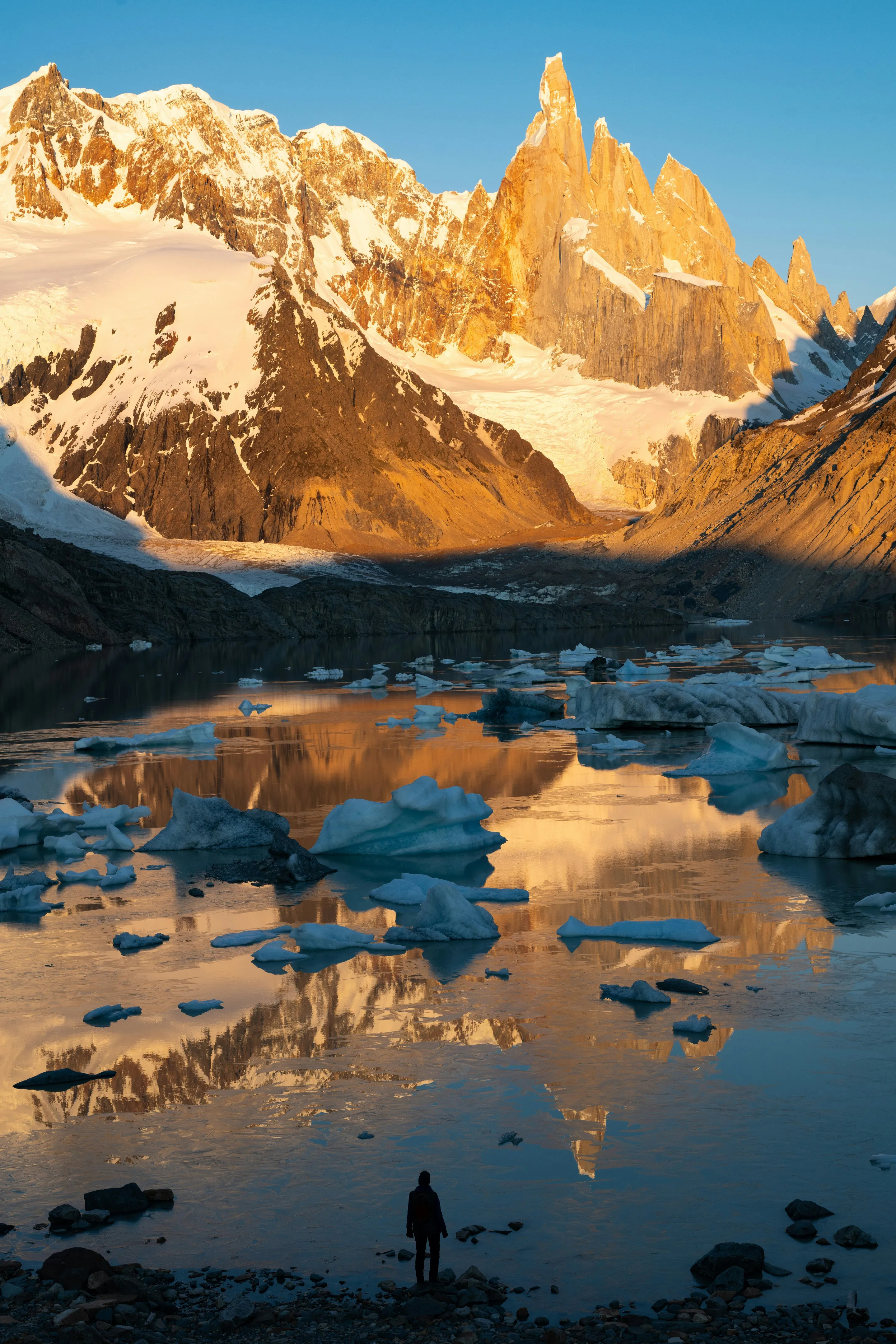 Golden sunrise on Cerro Torre reflected across an icy lake